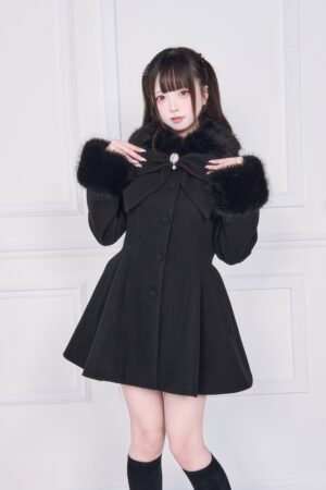 Pure black Jirai Kei winter coat with black faux fur collar and cuff trims, statement front bow decoration, modeled with black thigh-high socks in white studio