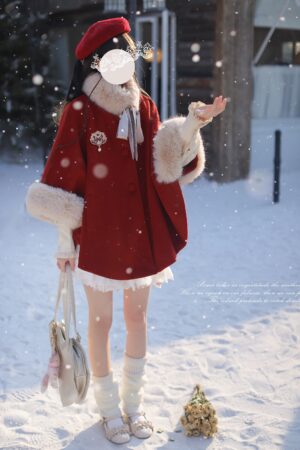 Red wool Jirai Kei cloak with elegant beige faux fur trim and decorative bow, styled with white lace mini skirt and heart-shaped handbag, front right three-quarter angle on snowy ground, complete Tenshi aesthetic outfit