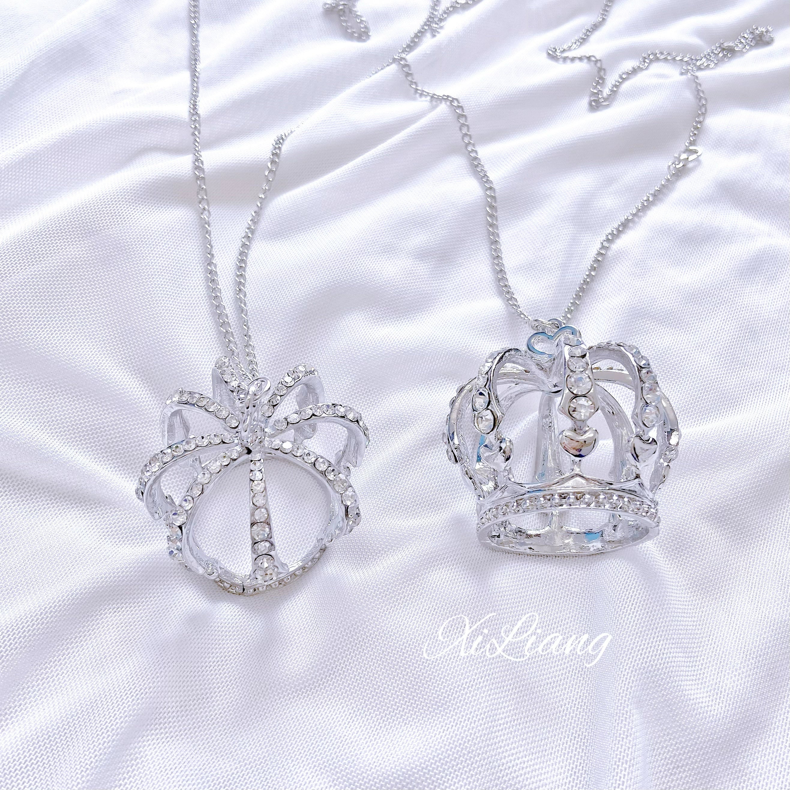Two styles of crown rhinestone necklaces on white satin background, silver tone hollow crown pendants decorated with sparkling rhinestones comparison style