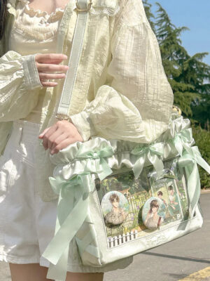 Mint chocolate Jirai Kei itabag close-up front view with transparent PVC display window showing round character badges and satin ribbon bows details on outdoor street