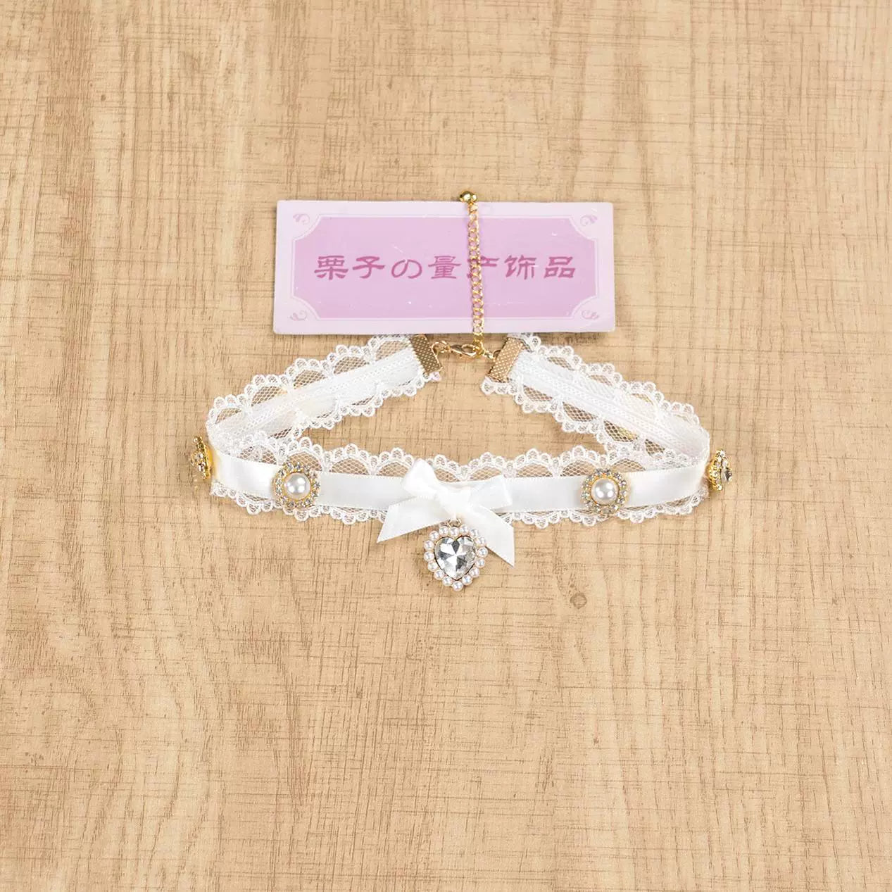 Pure white lace satin Jirai Kei choker necklace with central satin bow and heart rhinestone pendant on wooden table