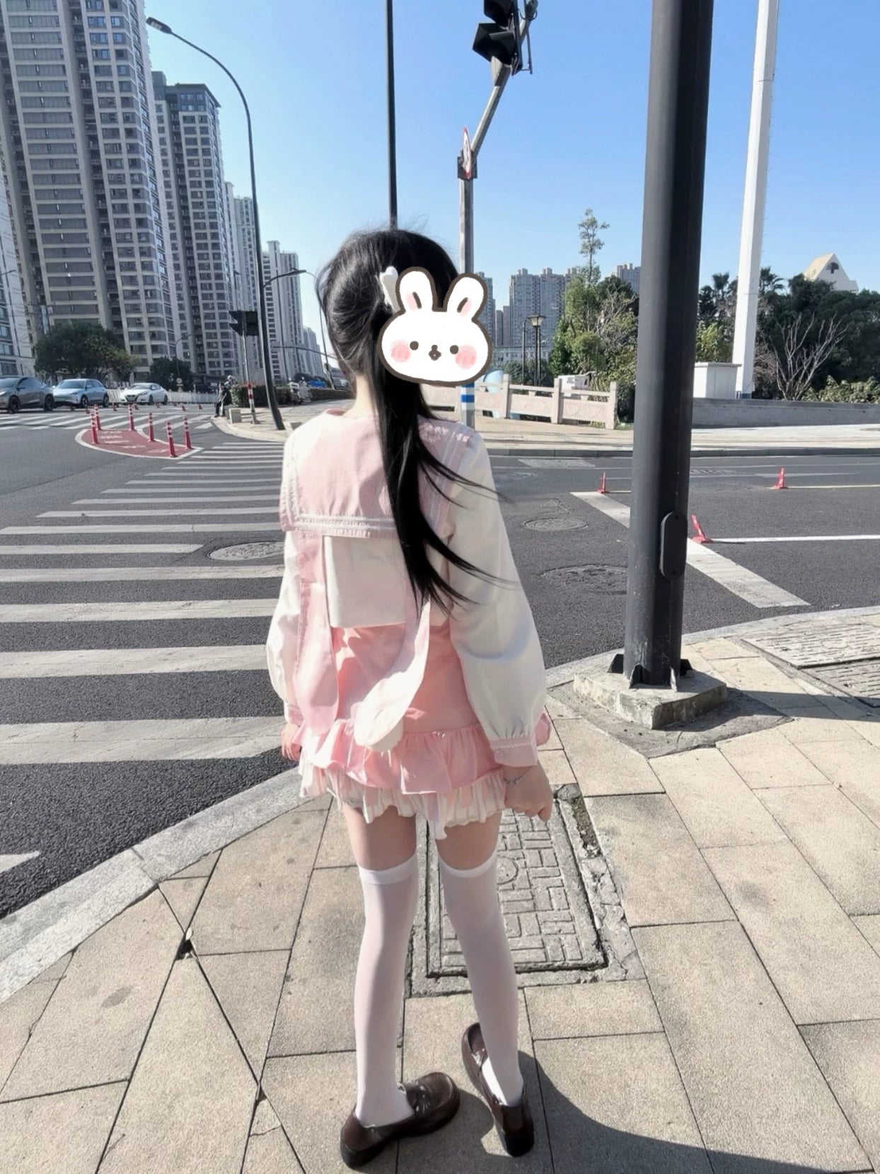 Back view of Jirai Kei sailor collar outfit with pink ruffle mini skirt, white thigh-high socks, brown Mary Jane loafers, and bunny sticker detail on urban sidewalk
