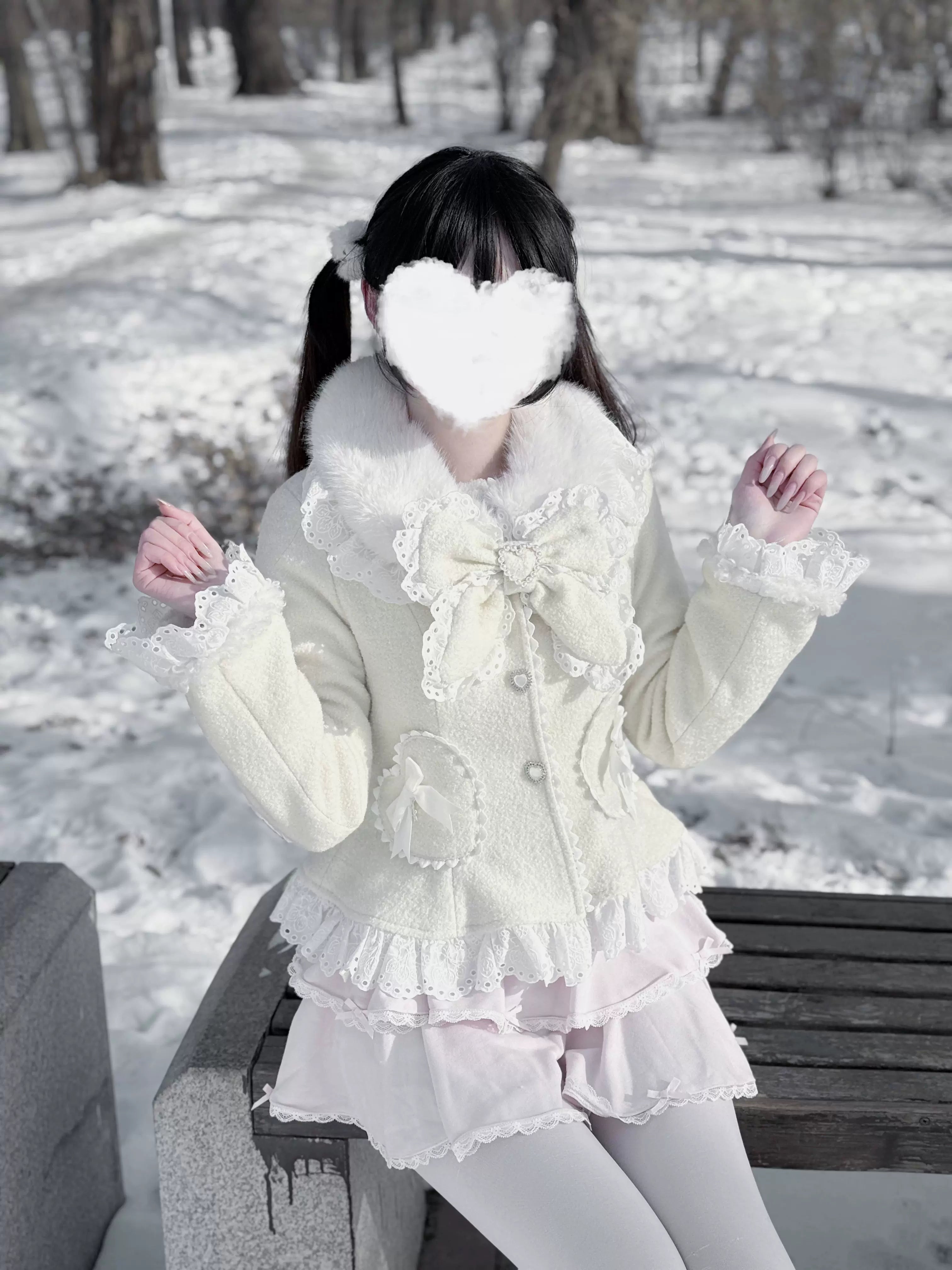 Cream off-white Ryousangata Jirai Kei coat with heart pockets and fuzzy faux fur collar, close-up eye-level view on model sitting in snowy outdoor park