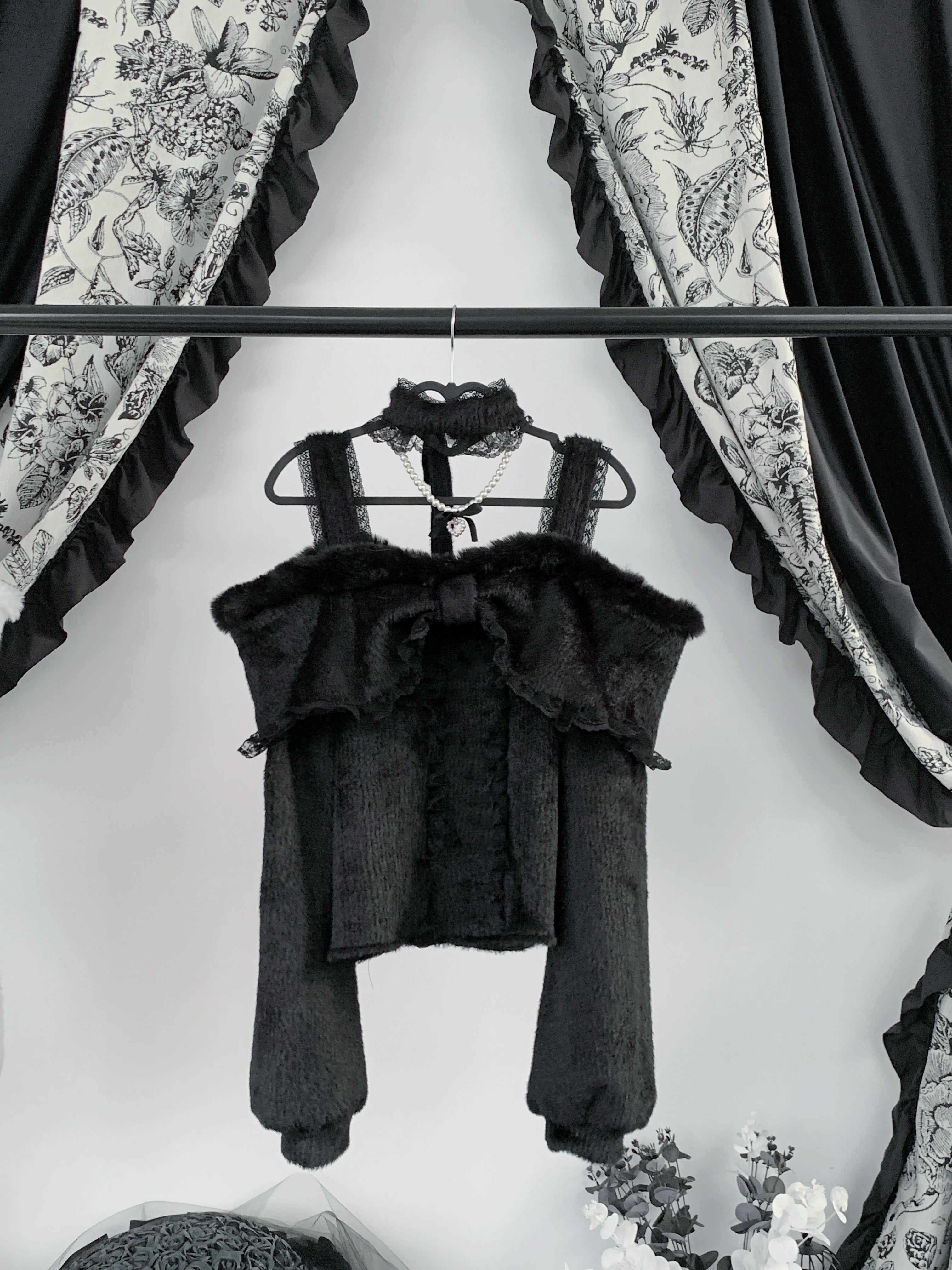 Black off-shoulder plush fleece top with large front bow and attached pearl choker, showcasing fuzzy fabric texture and dramatic silhouette