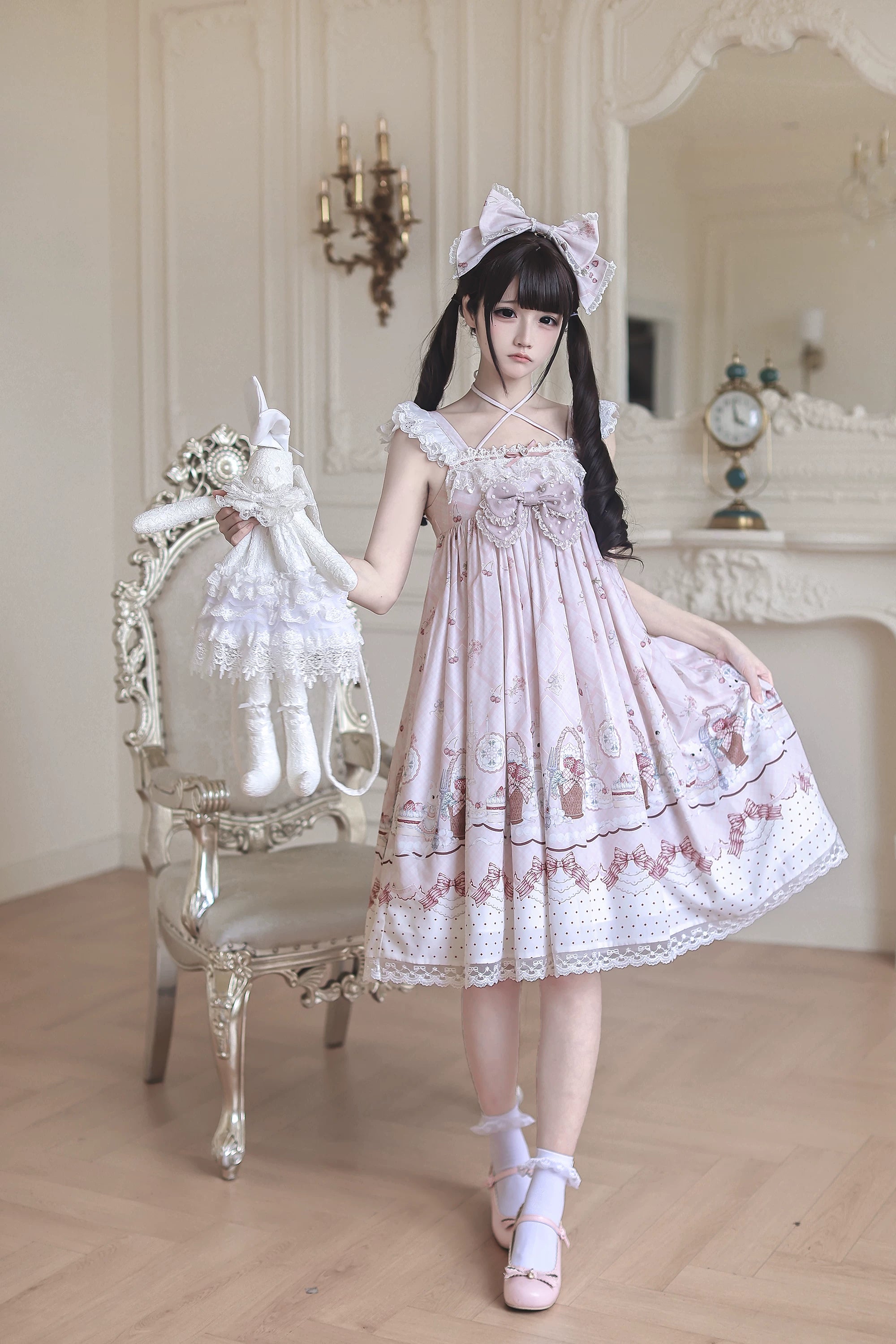 Side-front three-quarter view of strawberry bunny Jirai Kei Lolita dress with ruffled straps model holding lace rabbit doll lace hem and matching hair accessories