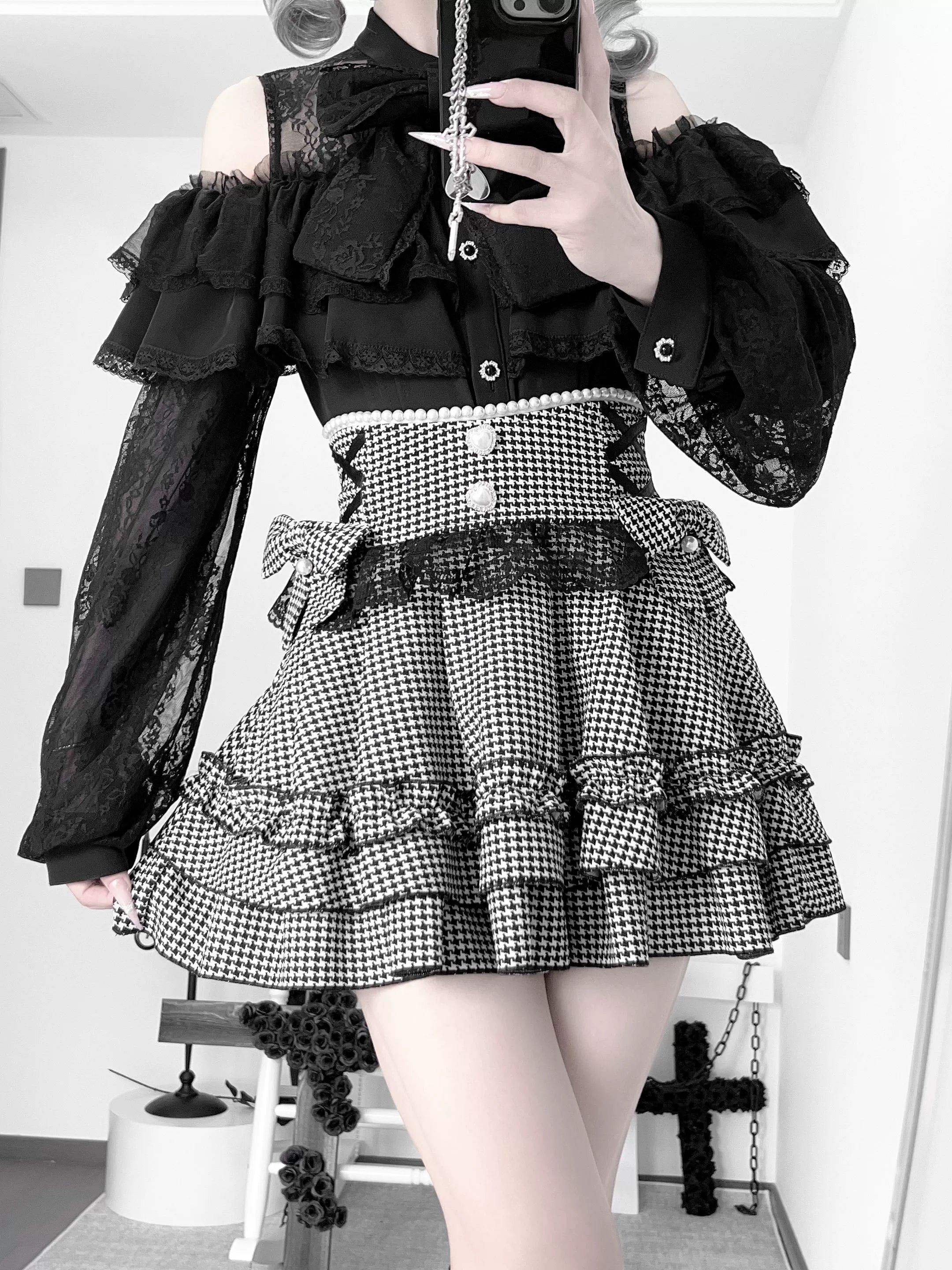 Black houndstooth jirai kei ruffle skirt with detachable bow worn with off-shoulder lace blouse, front half-body view showing layered ruffled hem and buttoned waist