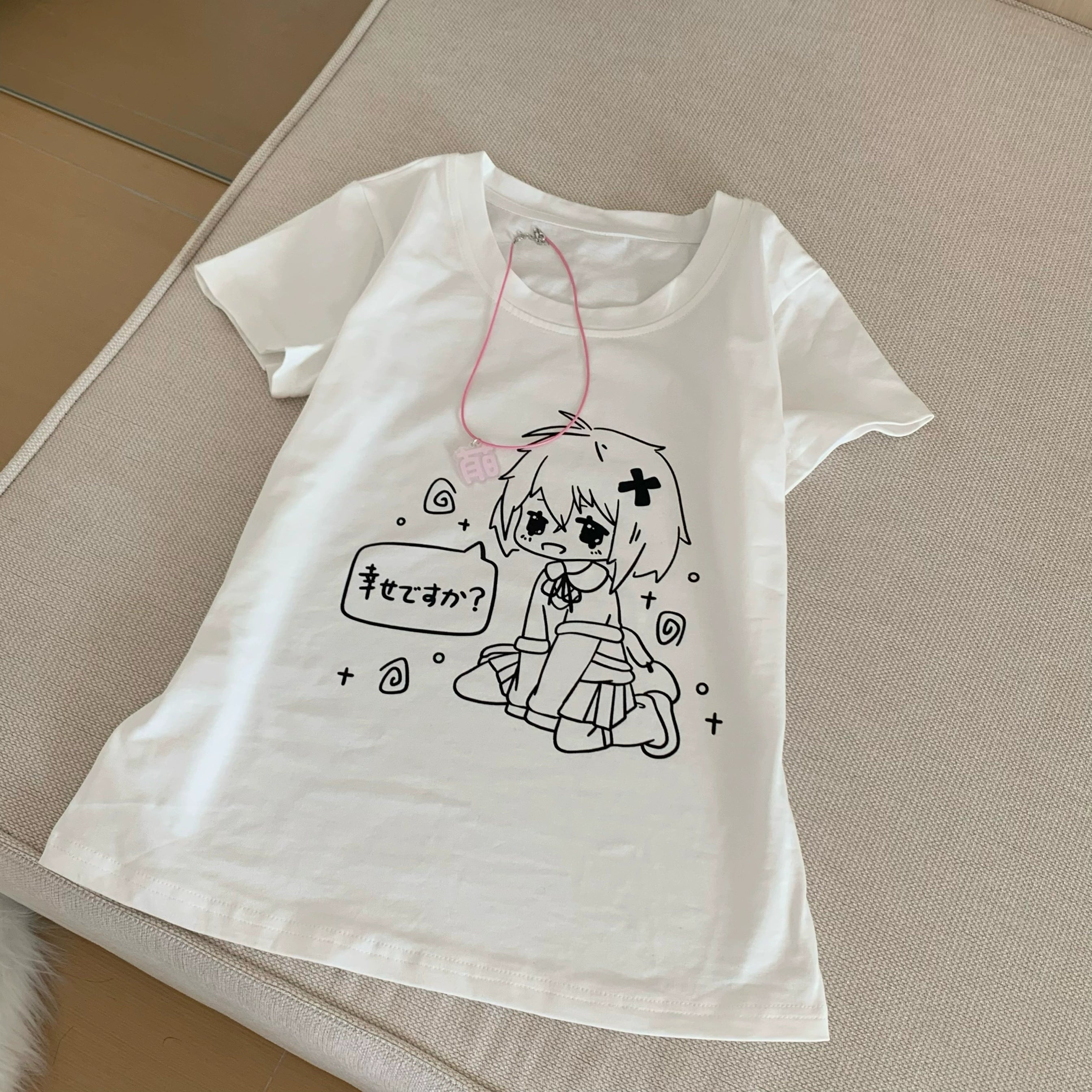 White anime graphic t-shirt flat lay overhead view on bed showing print detail and product tag accessories