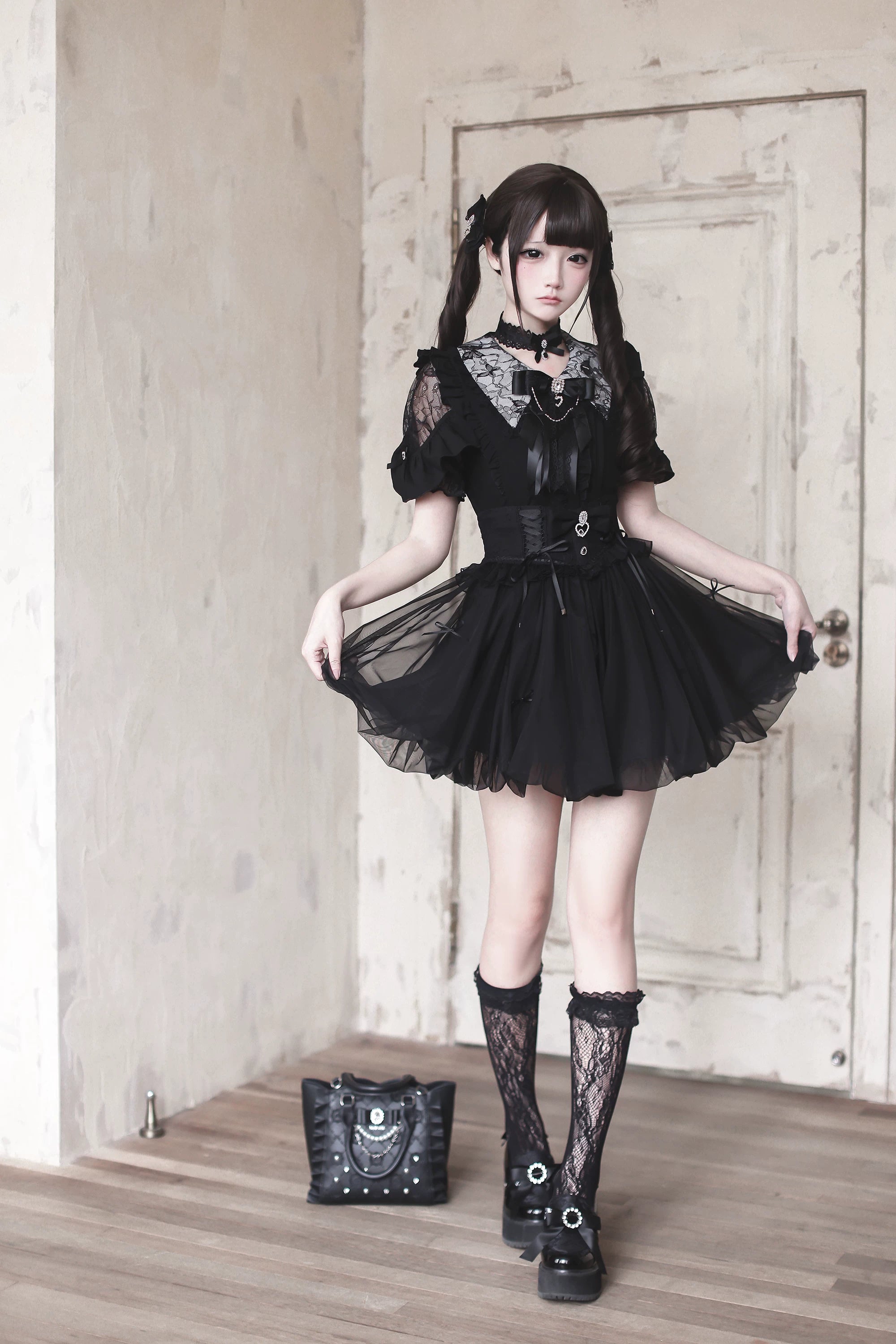 Black Jirai Kei bubble mini skirt worn on model with twin tails, lace collar and bow neck decoration, full body standing pose against vintage door backdrop
