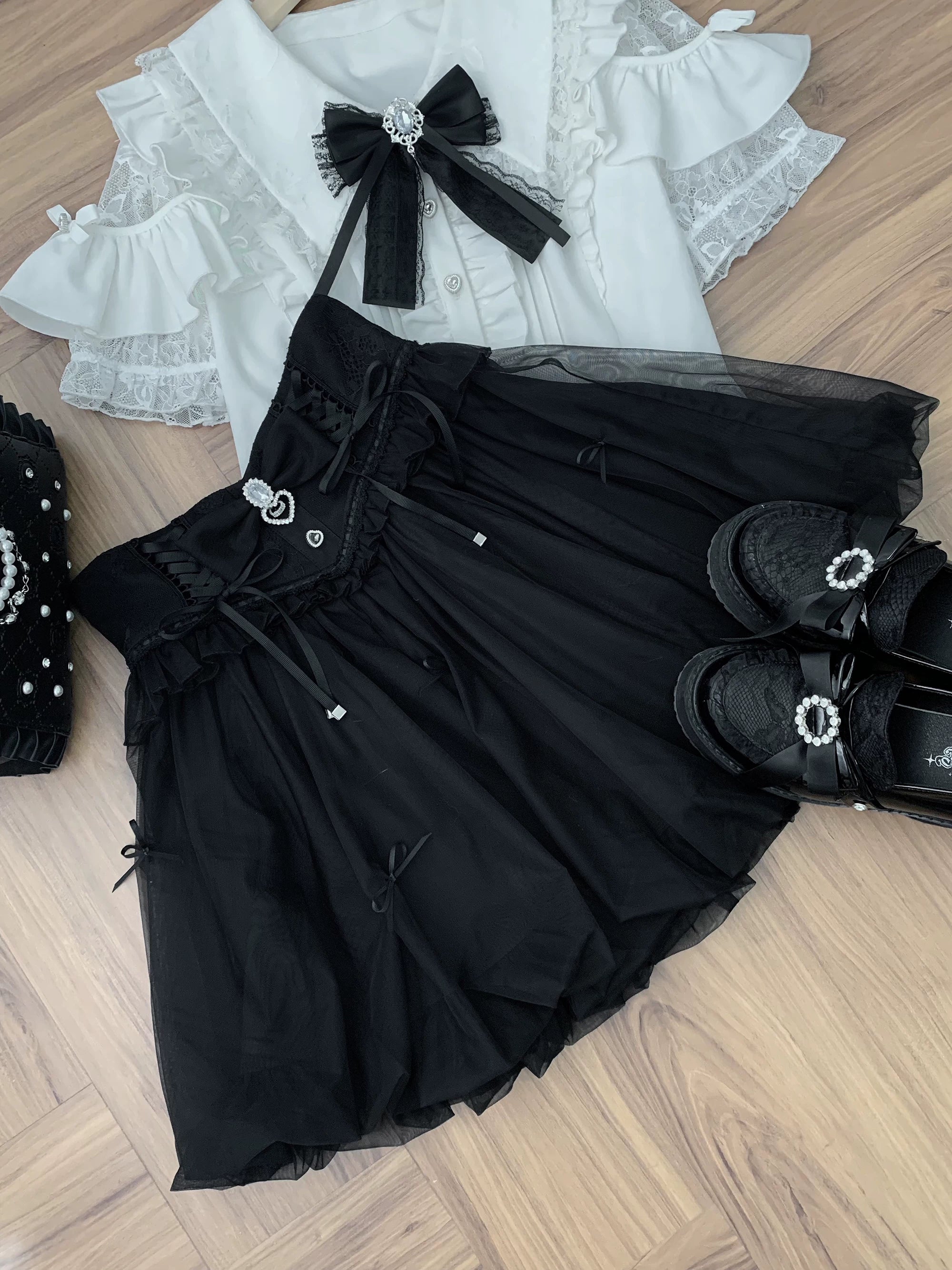 Black Jirai Kei bubble skirt with rhinestone trim and detachable bow, flat lay styling with coordinating accessories on wooden floor