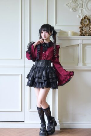 Burgundy Jirai Kei blouse with detachable princess trumpet sleeves and ruffled frills worn with black high-waisted skirt on vintage paneled wall backdrop