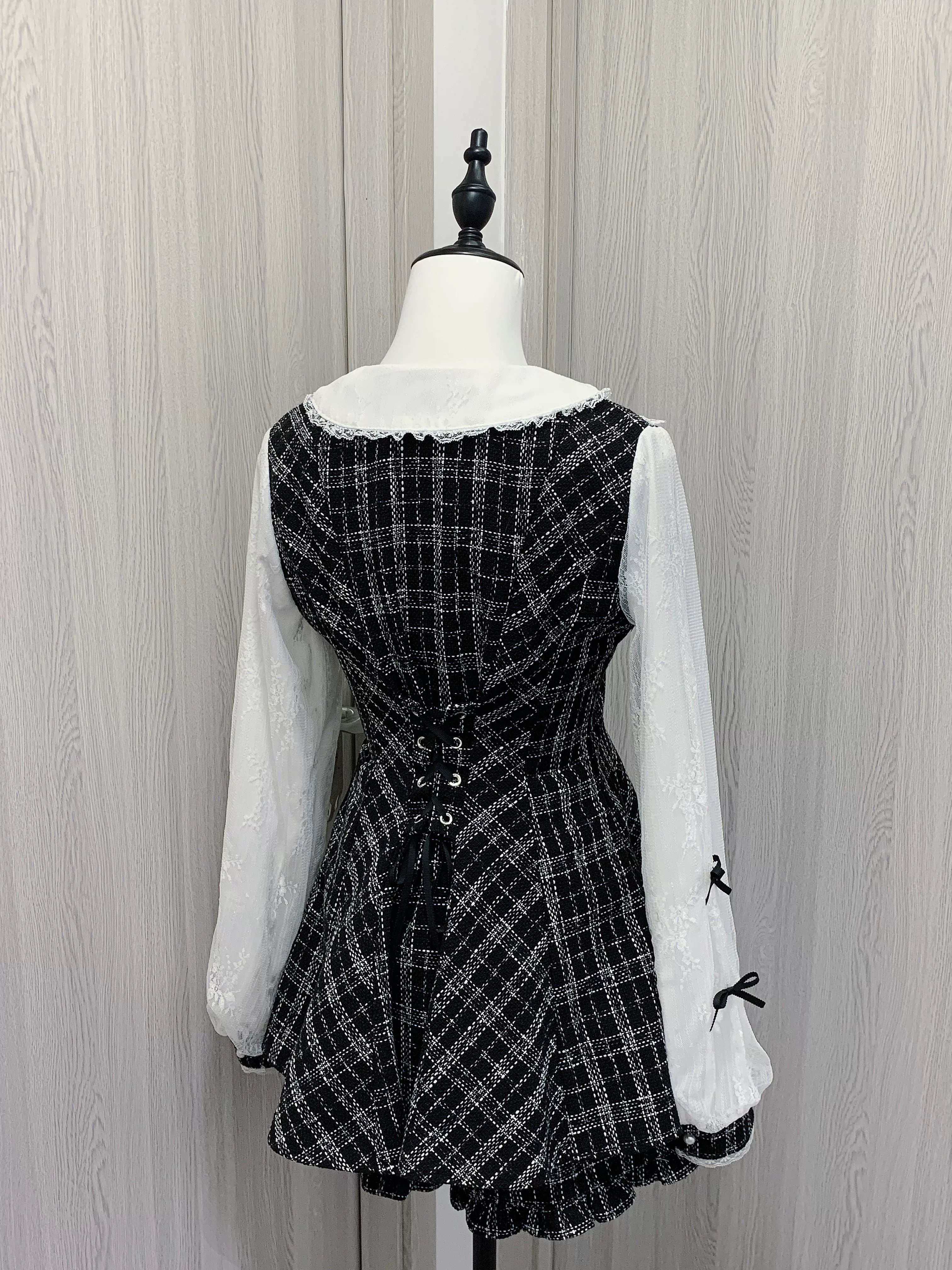 Rear view of black and white plaid Jirai Kei dress highlighting lace-up back design, double-layer chiffon sleeves with bow details, and ruffle hem shorts back panel