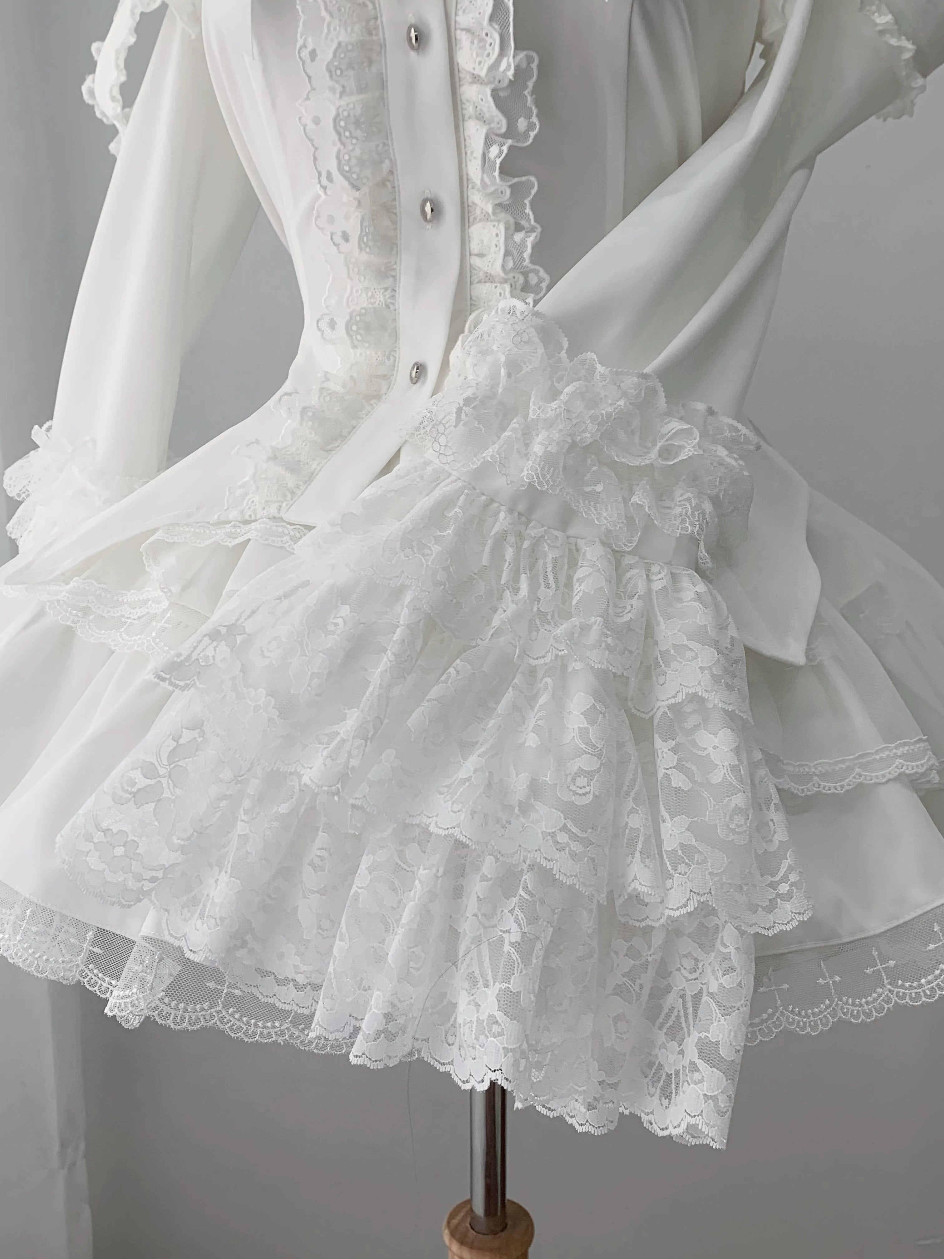 White lolita outfit layered lace ruffled hem and corset-style button front with satin fabric finish close-up detail