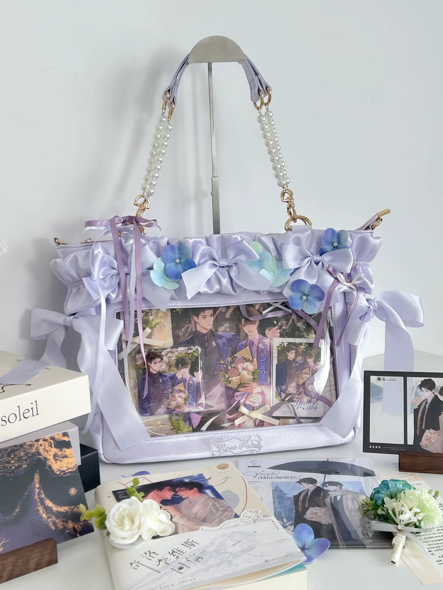 Lavender purple Jirai Kei itabag flat lay front view indoor setting flower decorations ruffled trims pearl top handle clear photo window display