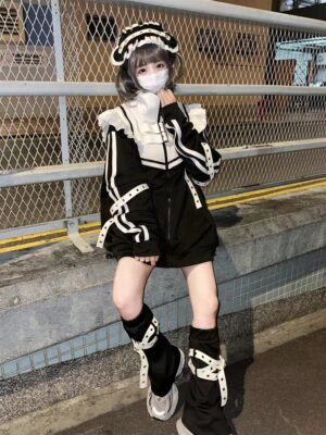 Black and white Tenshi Kaiwai gothic jacket outfit on masked model, outdoor street railing location, maid-style collar with cross strap trims and loose black shorts, full-body front view