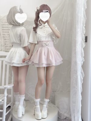 Two female models wearing matching Ryousangata lolita two-piece outfits with white blouse and pink ruffled skirt, shown in mirror selfie rear-side view with sheer lace curtains