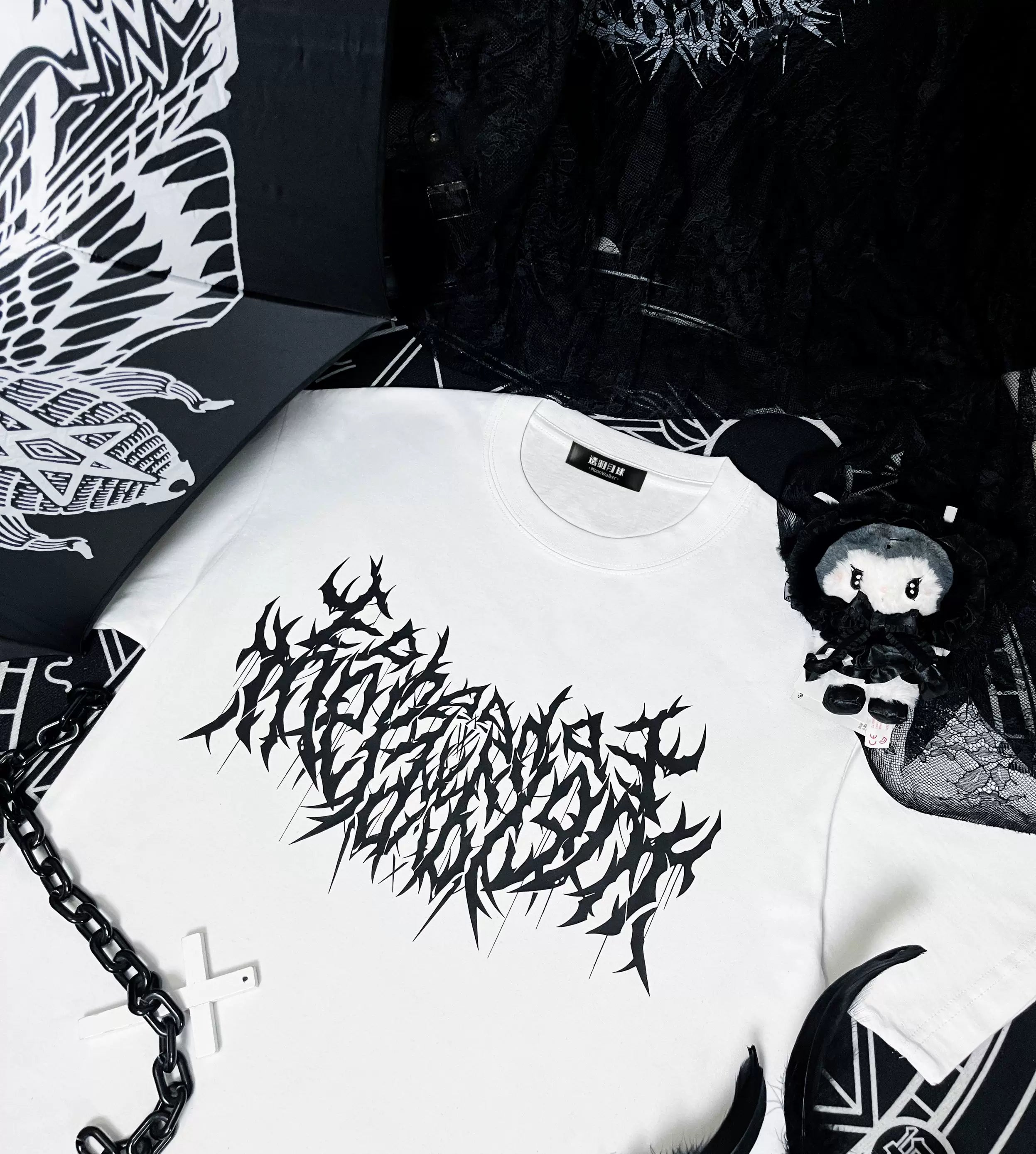 White oversized gothic print cotton t-shirt jirai kei flat lay with cross chain accessory and plush pendant styling