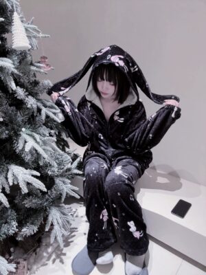 Black-pink angel bunny ear hooded pajamas set with white celestial prints and musical notes, worn by model in Christmas setting showcasing front three-quarter view