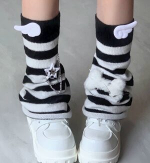 Close-up detail of black and white striped leg warmers featuring angel wing charm fluffy bow and star chain embellishments with platform loafers