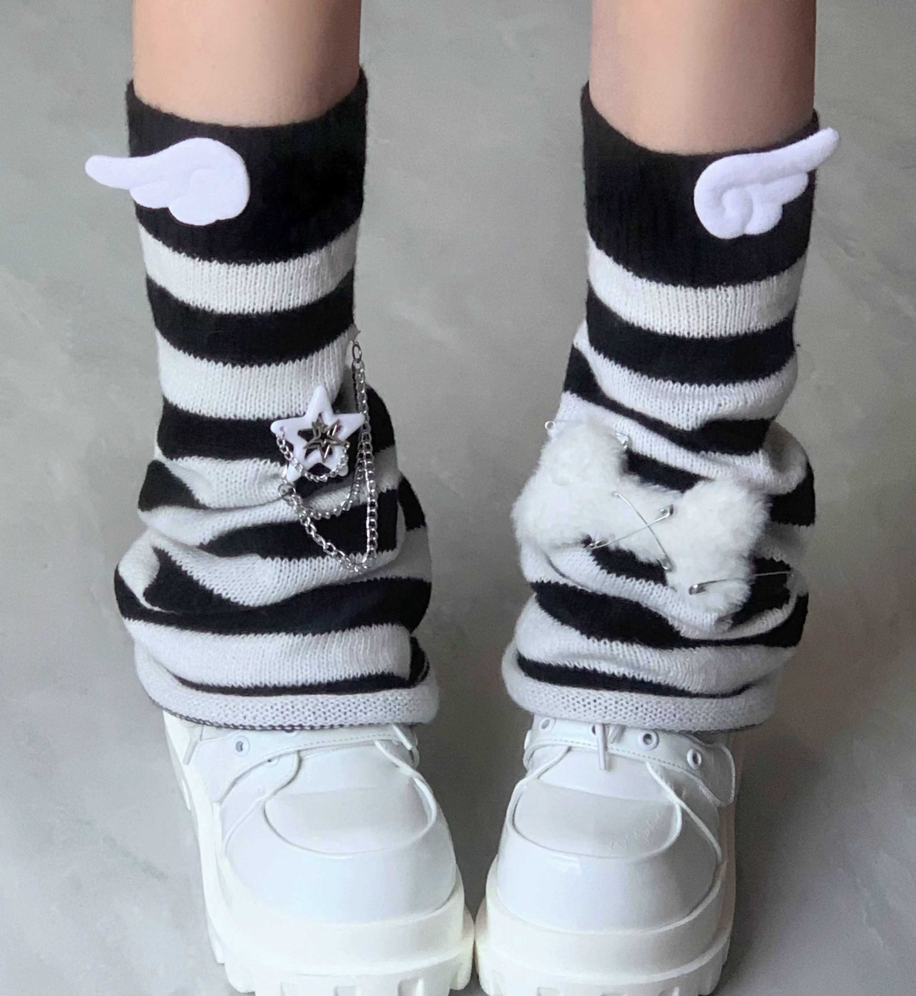 Close-up detail of black and white striped leg warmers featuring angel wing charm fluffy bow and star chain embellishments with platform loafers