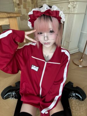 Pink-haired model wearing maroon and white jirai kei track jacket with maid headband aesthetic, front three-quarter view showcasing white sleeve stripes and embroidered name tag detail, vintage Japanese schoolgirl inspired fashion