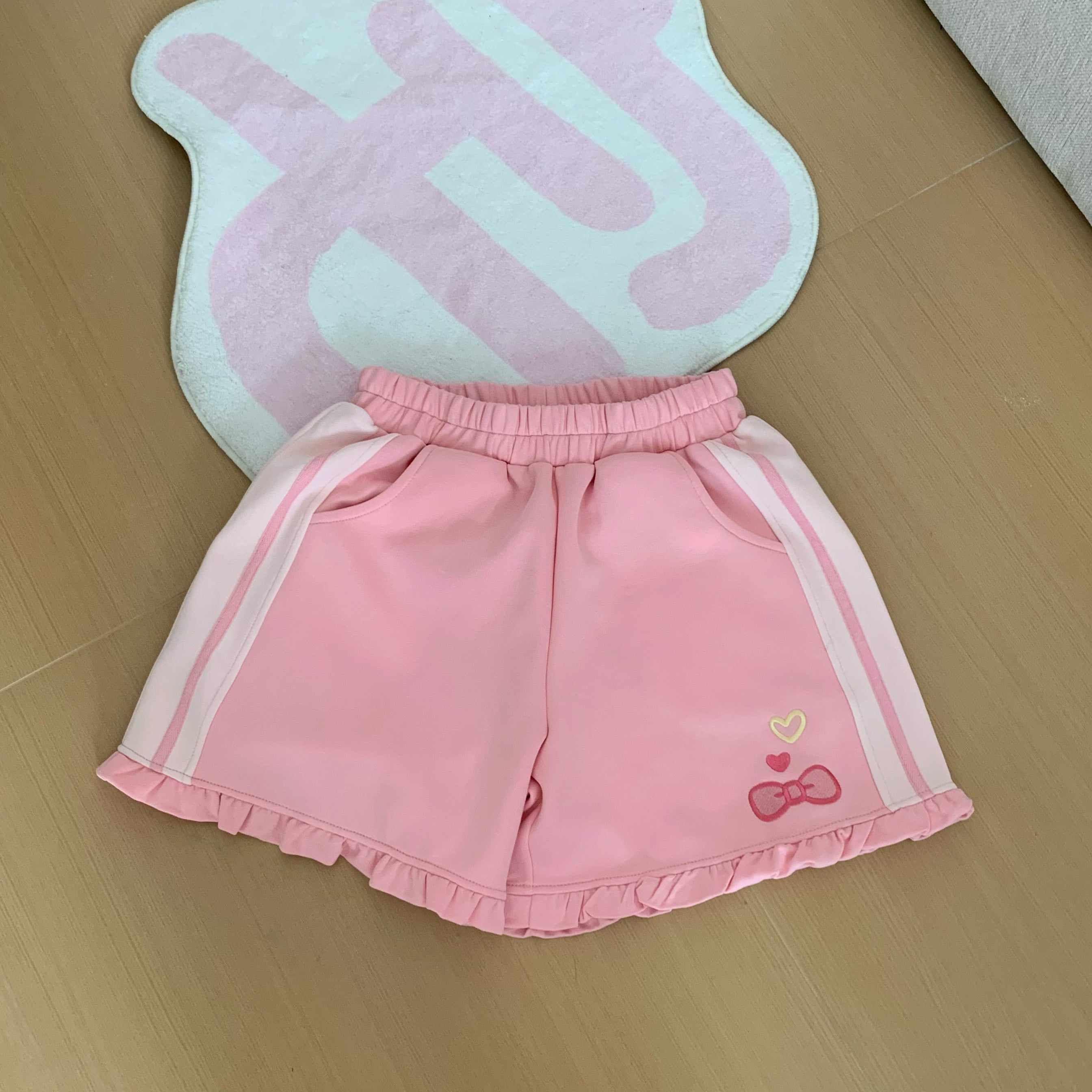 Jirai Kei pink strawberry embroidered shorts with elastic waistband, bow embroidery accent, side pockets, and ruffled hem detail, flat lay product showcase