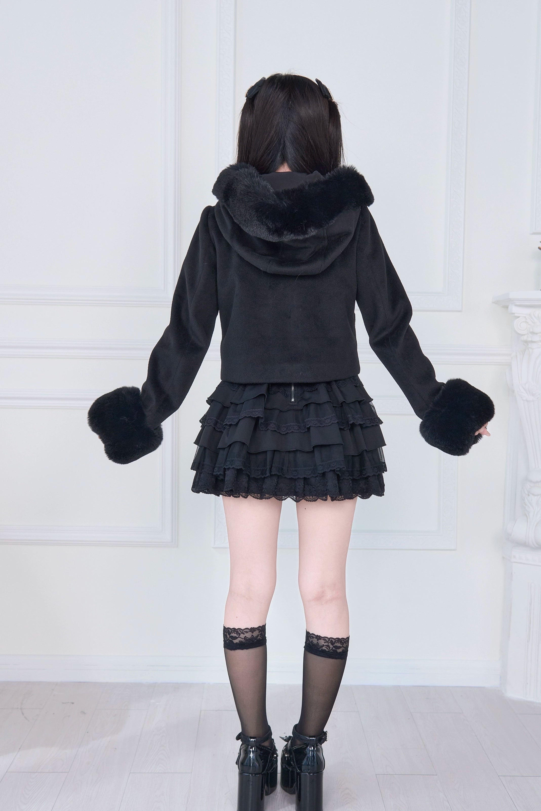 Black hooded rousangata coat back full-body model view, dark hair model with black ruffle skirt and black socks, rear silhouette showing coat length and hood design of jirai kei jacket