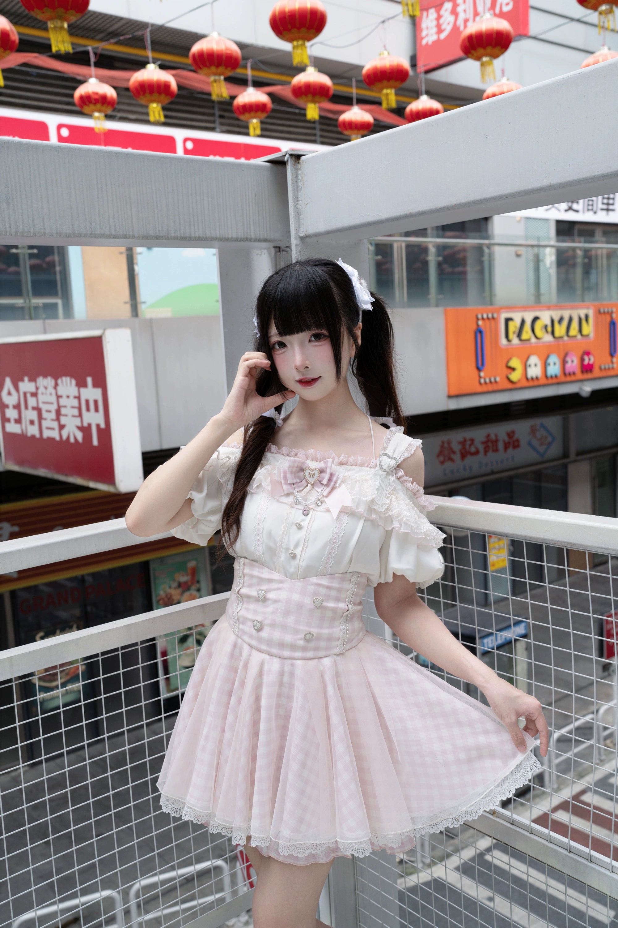 Three-quarter view of ryousangata ensemble with off-shoulder ruffle blouse pink gingham mini skirt and white platform heels outdoor balcony commercial setting