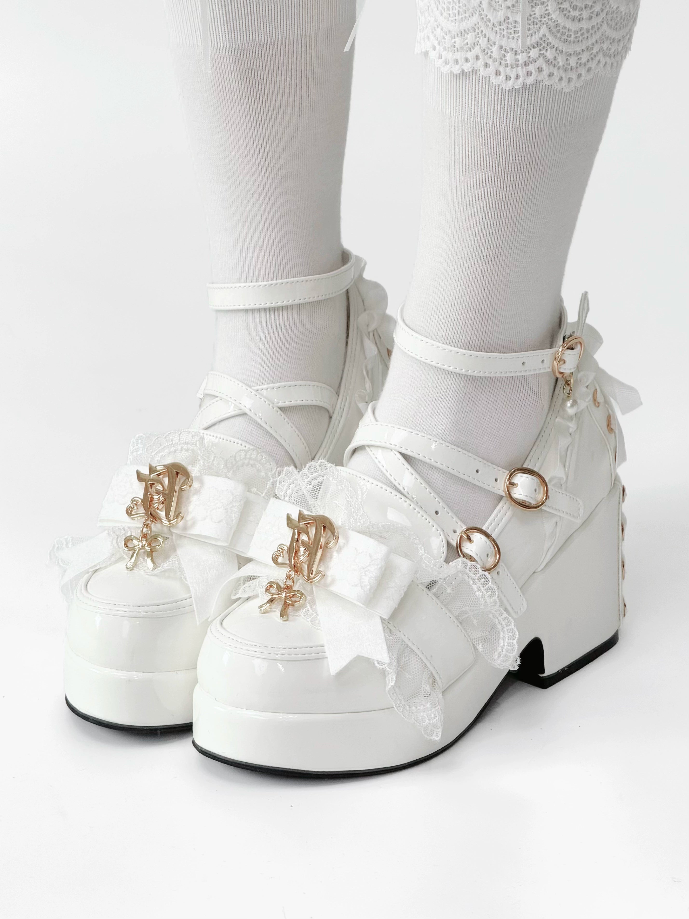 Front-side angle of white patent leather Jirai Kei platform heels on feet with white ruffled knee socks showing front lace bow thick block platform and gold logo charms