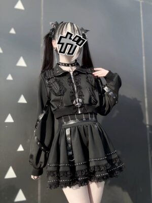 Black gothic punk jacket with cross zipper and studded mini skirt paired with leg warmers front medium shot triangle pattern wall background