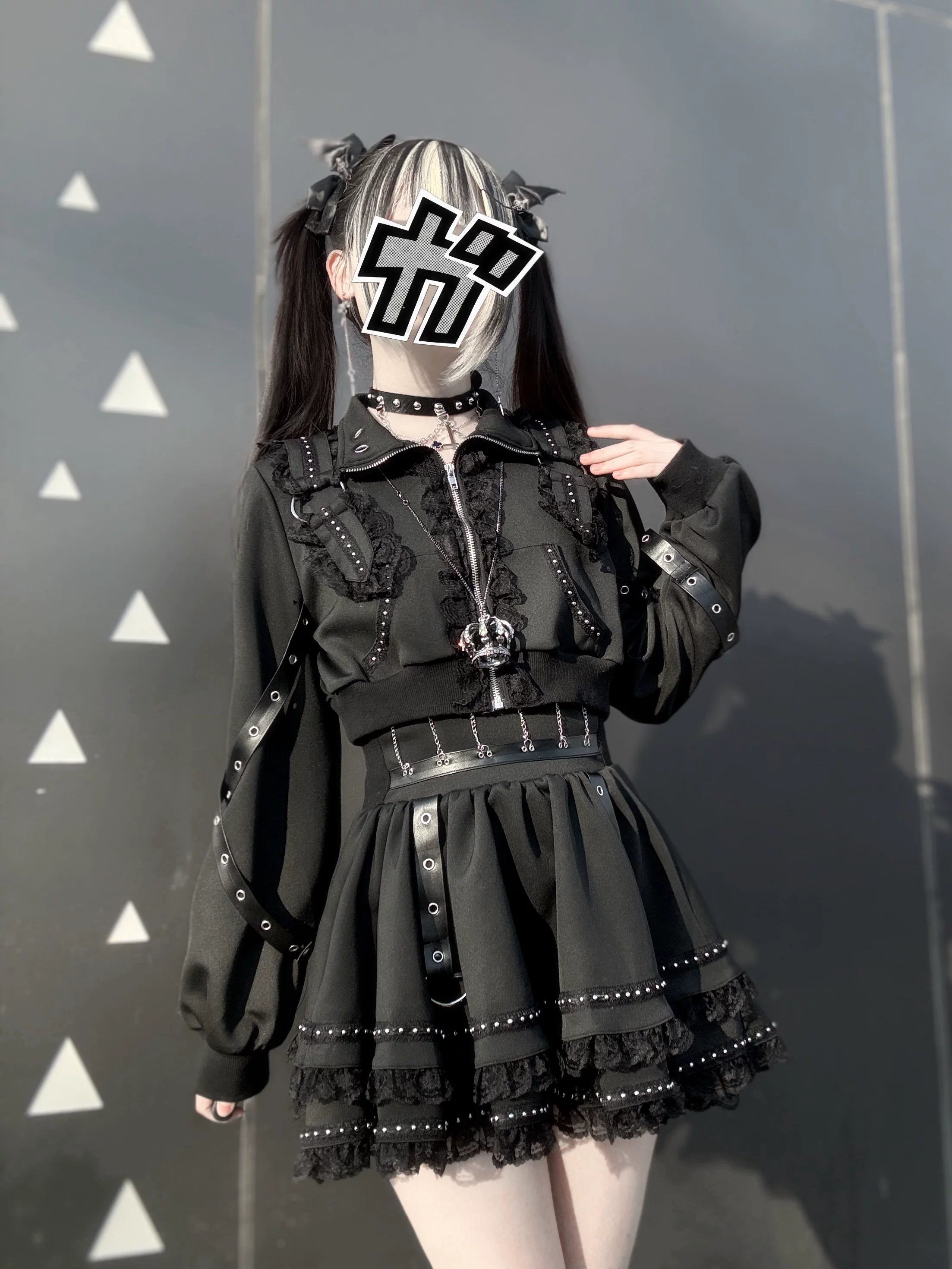Black gothic punk jacket with cross zipper and studded mini skirt paired with leg warmers front medium shot triangle pattern wall background