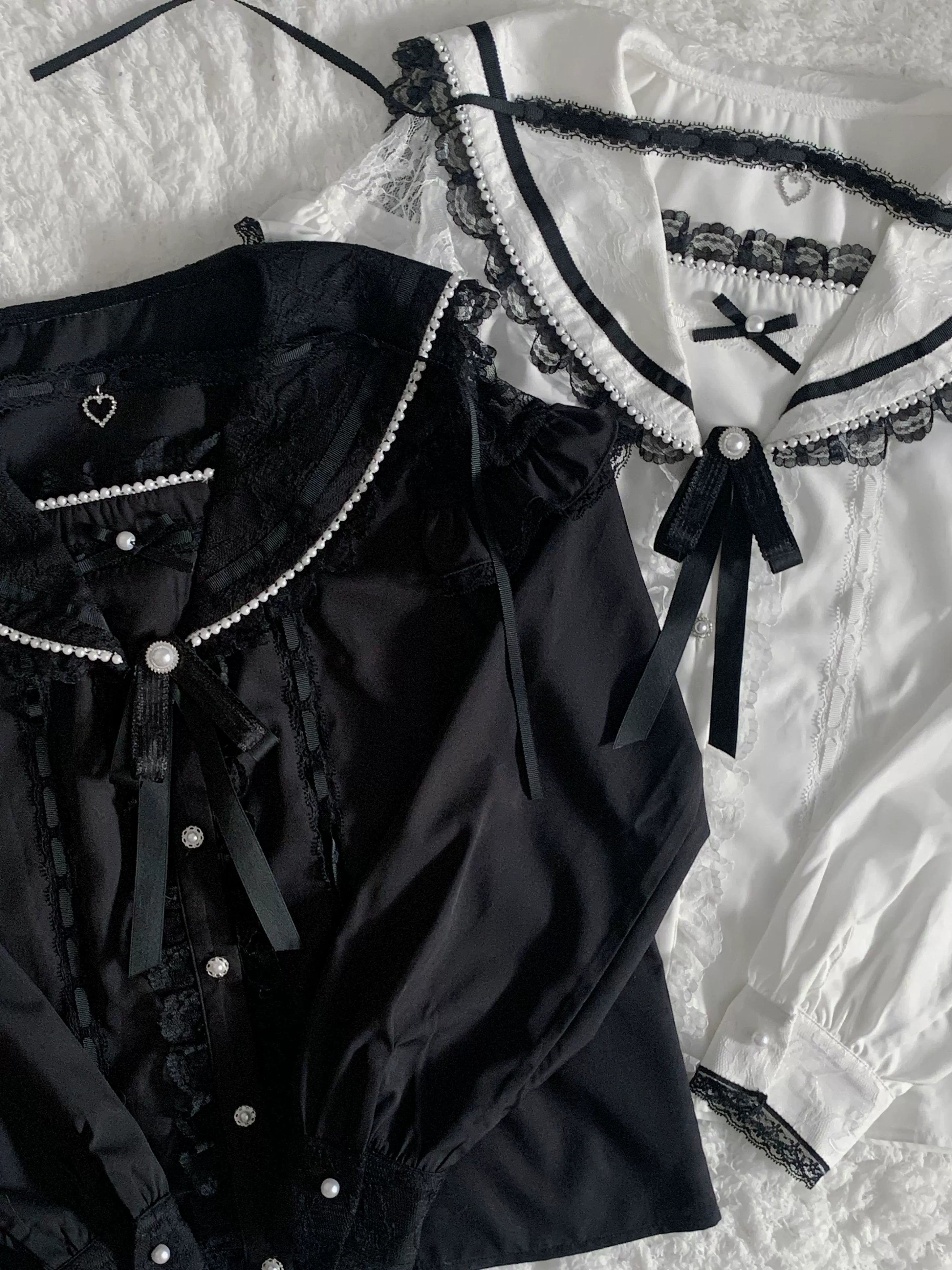 Flat studio close-up view of black and white Jirai Kei sailor collar blouses displaying lace trim detailing, removable ribbon bow accents, pearl button closures, and architectural design elements from multiple angle perspectives