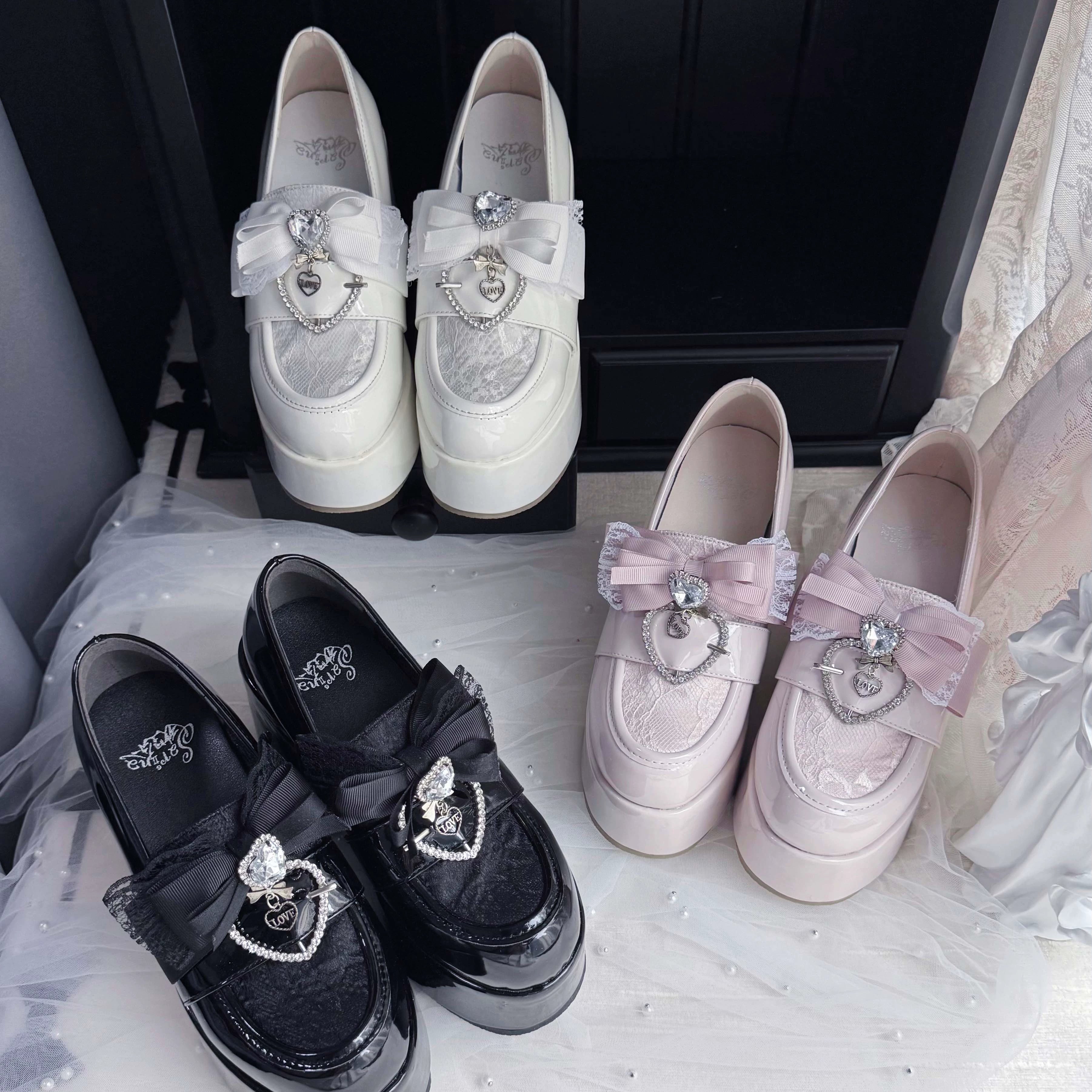 Four pairs of Ryousangata Jirai Kei platform loafers featuring two bow styles and heart rhinestone buckles, arranged on decorative lace fabric flat lay