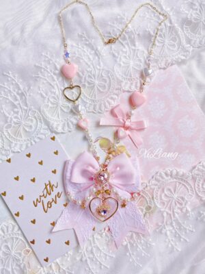 Pink Jirai Kei sweater chain necklace with gold heart charms and satin ribbon bow on white lace fabric backdrop, flat lay photography showing full length and delicate details