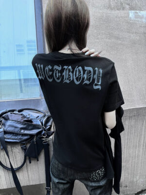 Black gothic printed jirai kei t-shirt back view on model with long hair outdoor street style wearing dark studded jeans and backpack displaying wetbody print