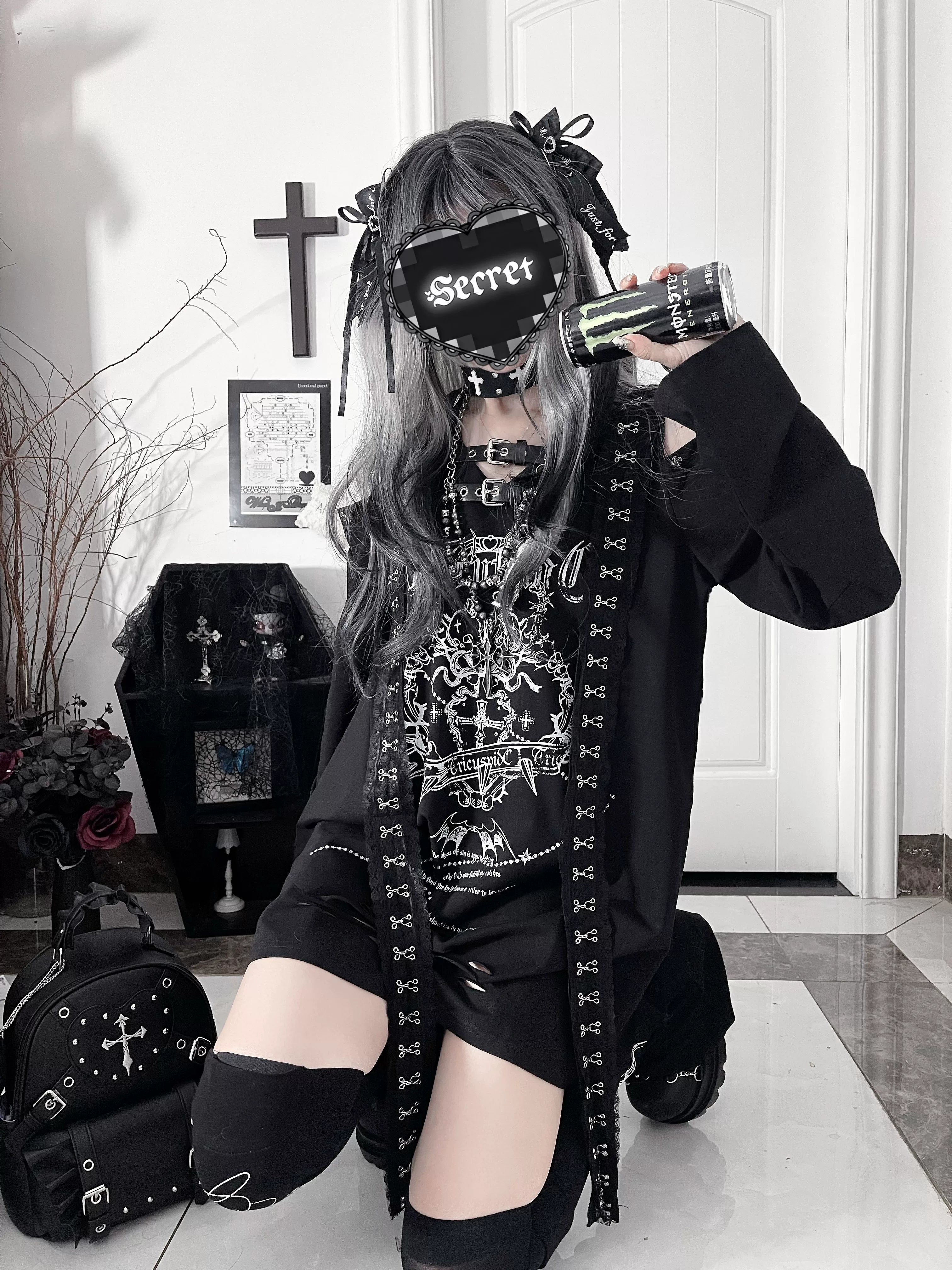 Full-length kneeling pose of black goth outfit set featuring distressed long-sleeve tee with cut-out shoulders and ripped hem, paired with single thigh-high sock and subculture accessories