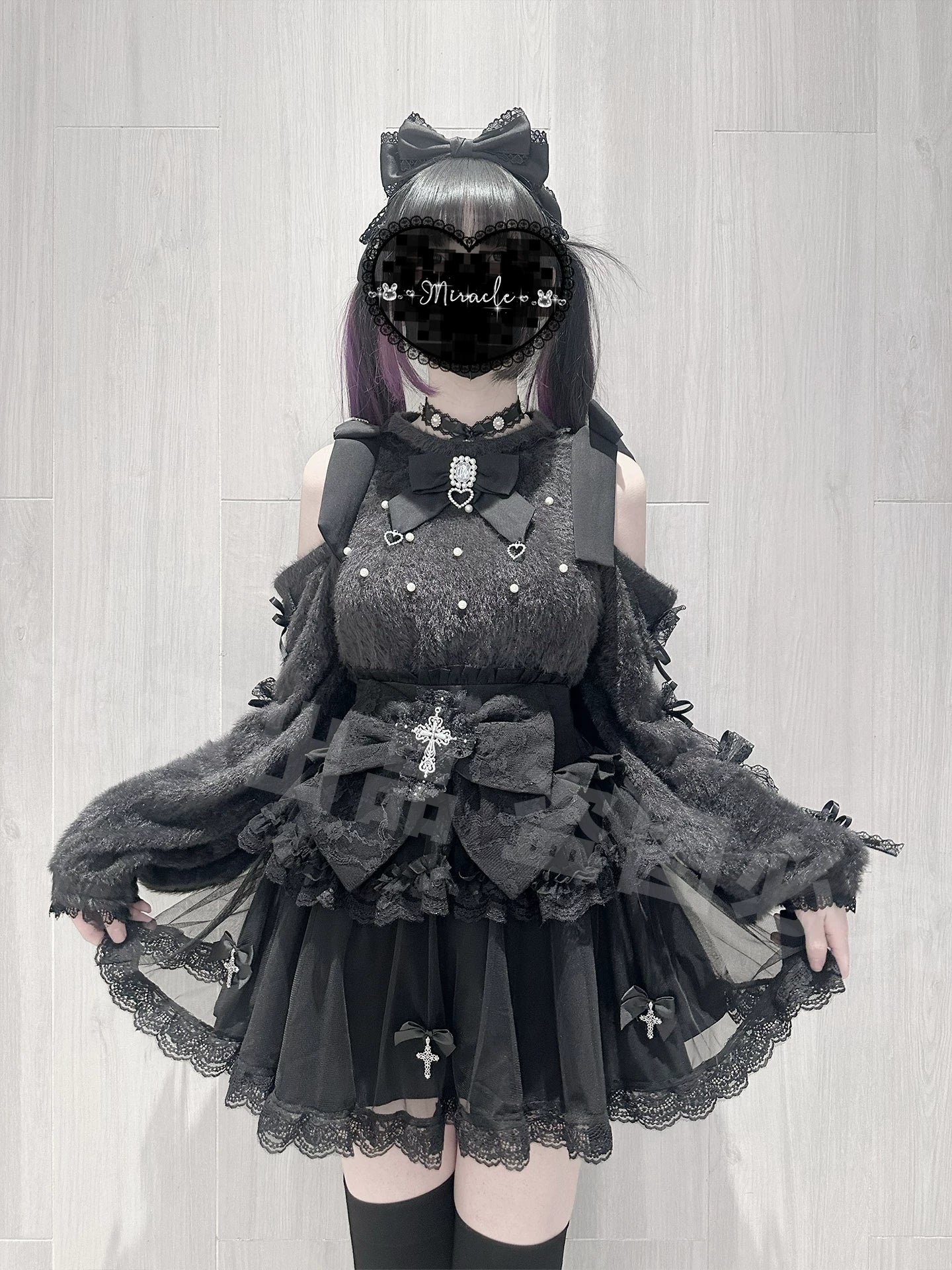 Flat mannequin display of black off-shoulder sweater with fuzzy fabric, large removable bow, cross ornament and pearl trim, paired with high-waist mini skirt showing construction details