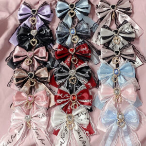 Overhead view of ryousangata bow hair accessories showing layered bow construction with rhinestone decorations and printed ribbon text on light pink fabric backdrop