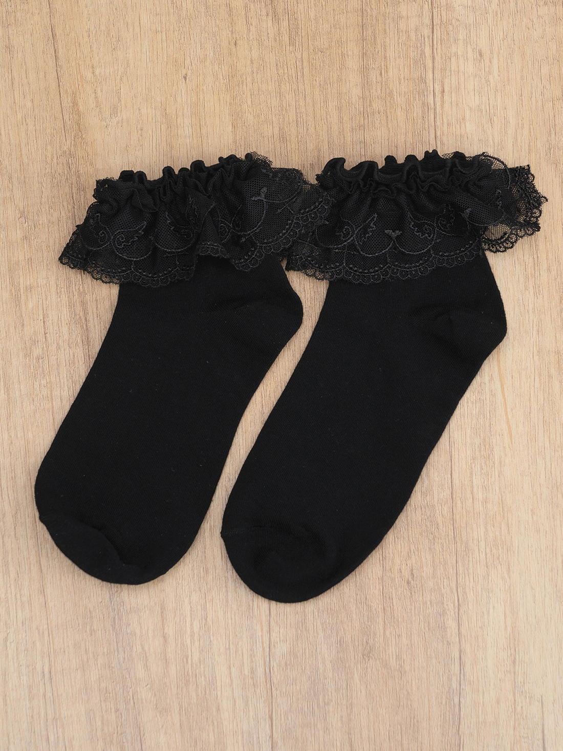 Pair of black Jirai Kei lace ruffle ankle socks flat lay top-down wood table background multi-layered ruffled lace cuffs