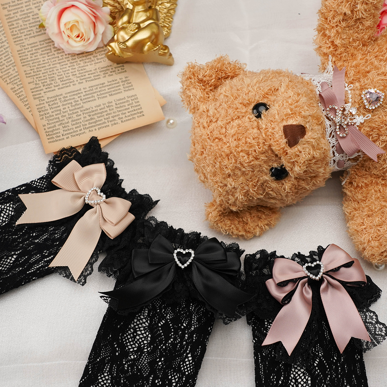 Top-down flat lay of black and pink jirai kei lace socks with heart-shaped rhinestone embellishments and black lace fabric styled with roses and vintage items