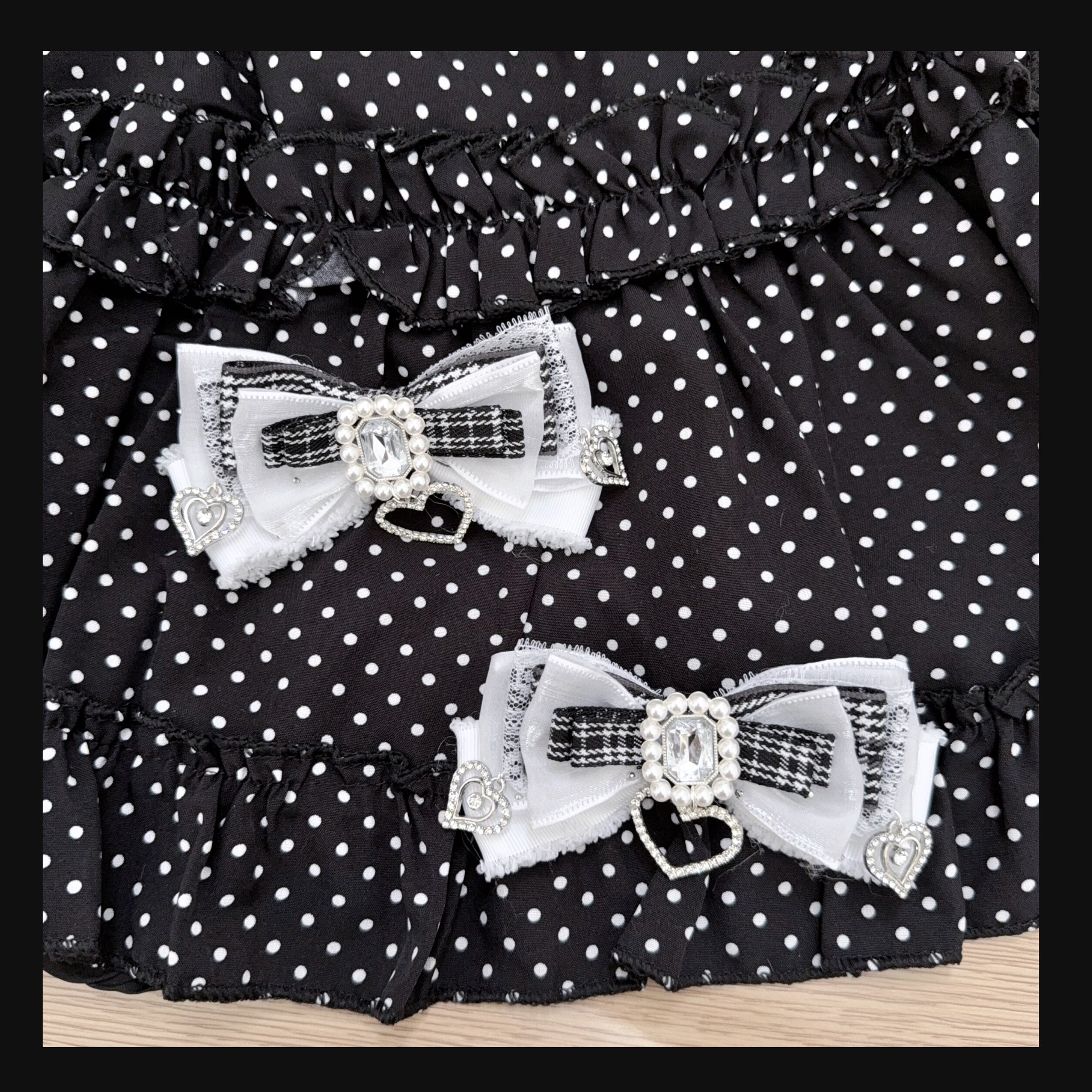 White and black houndstooth Jirai Kei bow hair clips with central rhinestone accents and heart-shaped charm pendants on polka dot backdrop