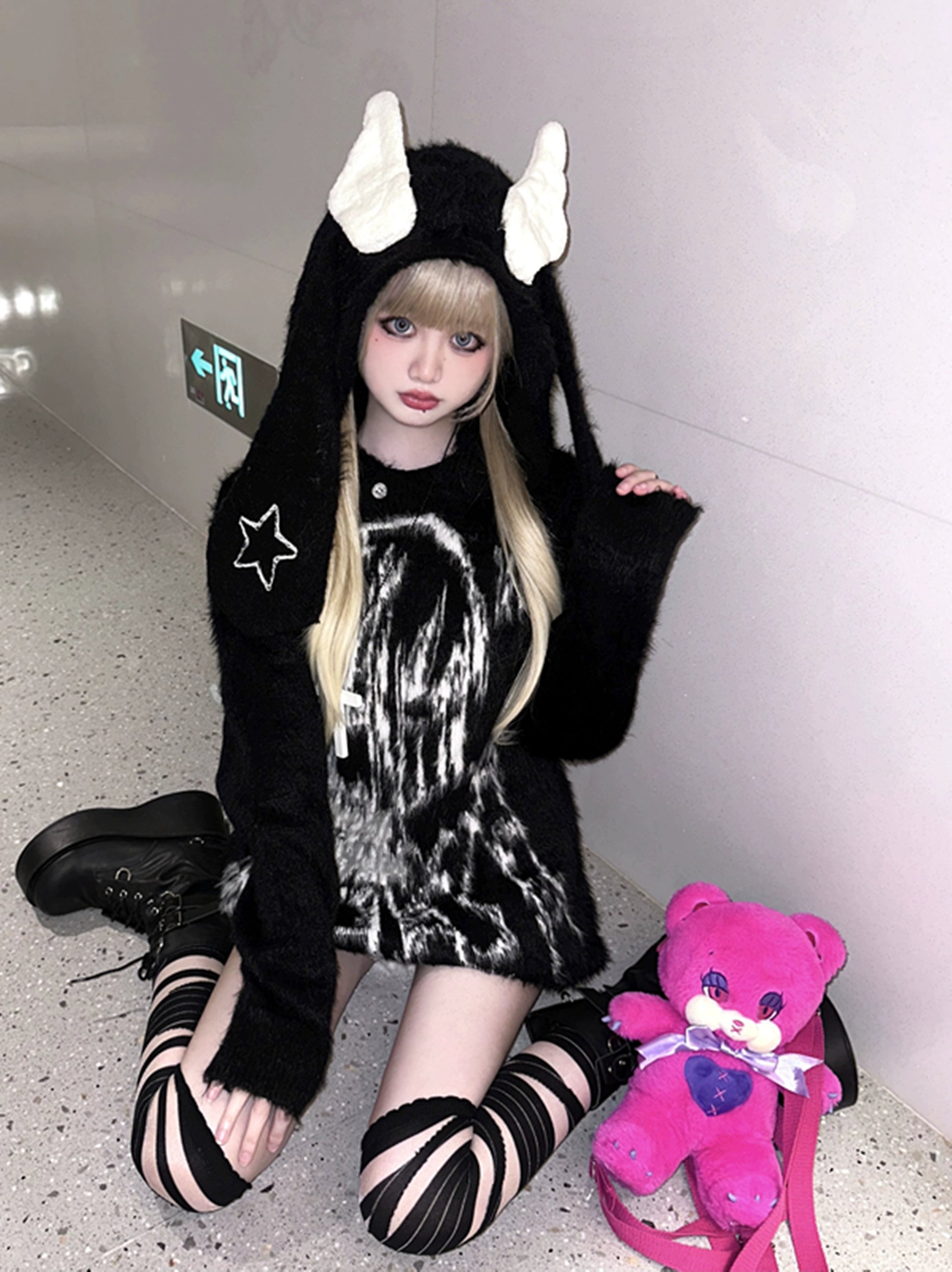 Black jirai kei bunny ear wing hooded sweater with star embroidery and anime ghost print worn in indoor elevator hallway with pink teddy bear styling
