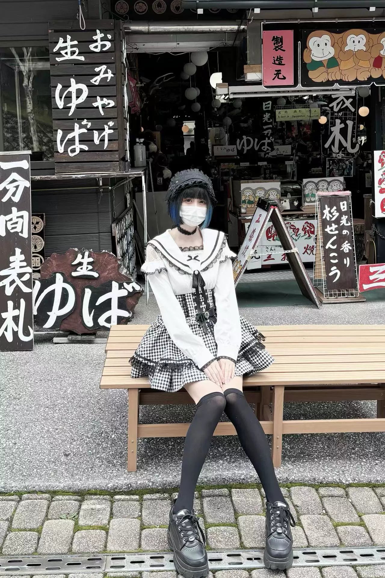 Masked female model sitting on outdoor bench wearing Jirai Kei sailor collar blouse outfit with thigh-high socks against Japanese street store background, capturing authentic street fashion context and urban aesthetic