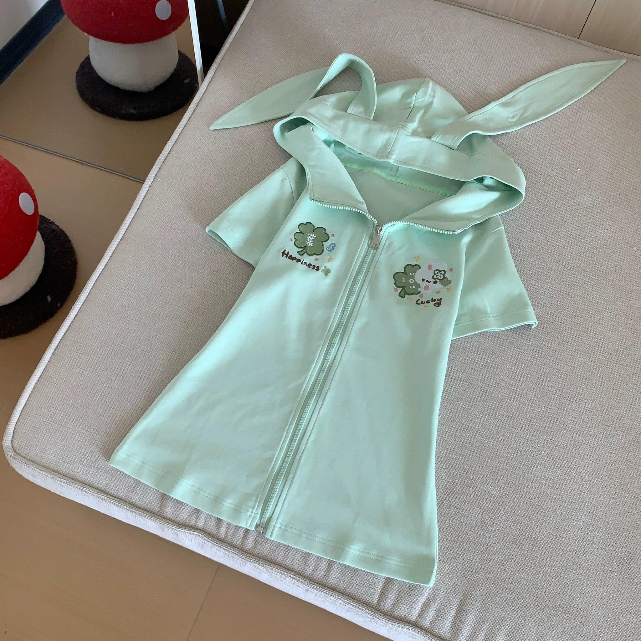 Mint green Jirai Kei short-sleeve zip-up sweatshirt with signature bunny ear hood design, front view on dress form showing slim fit construction and clover embroidery details