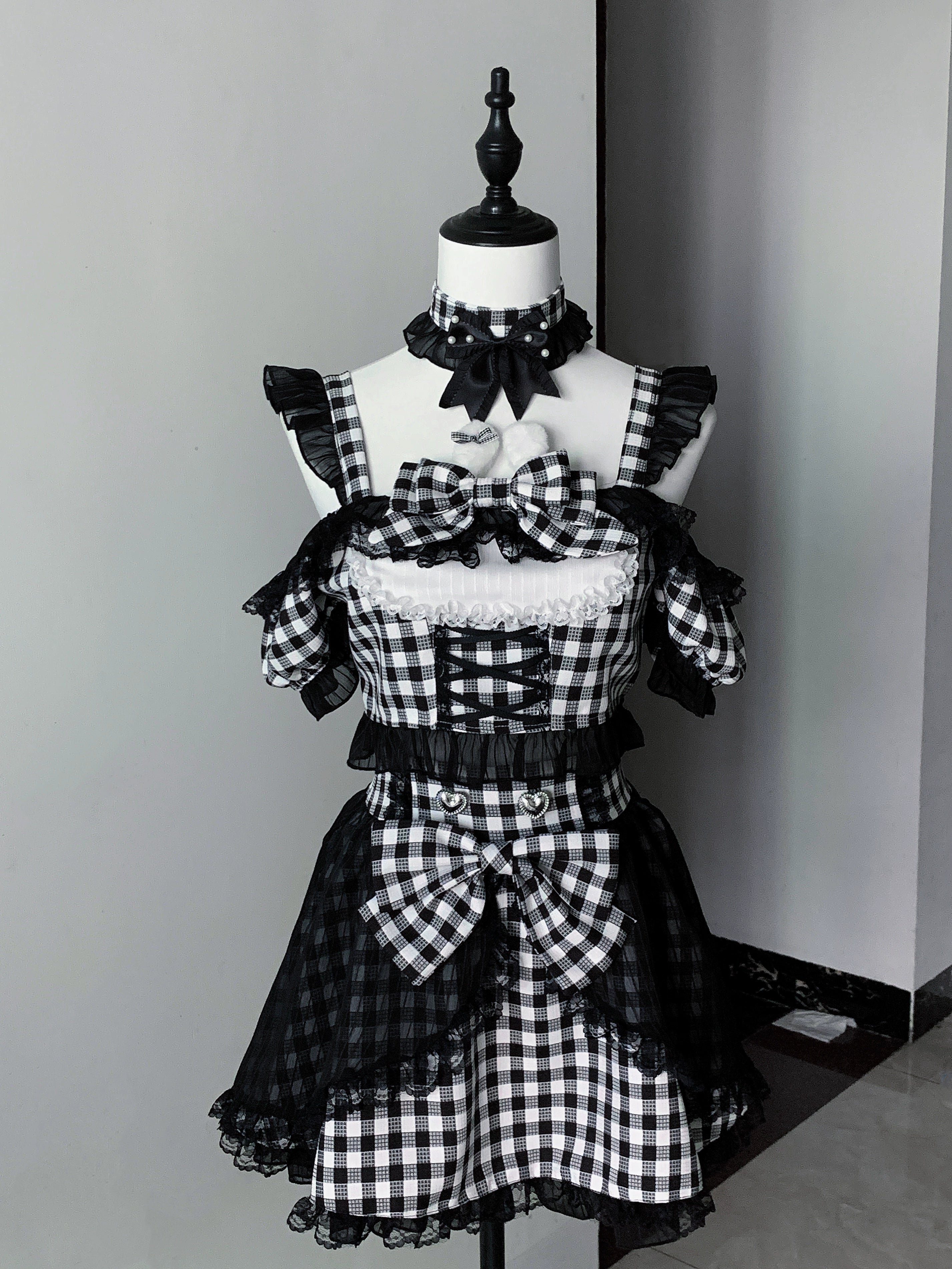 Black gingham jirai kei maid lolita outfit on mannequin display showing front large bow checkered layered skirt and cold-shoulder sleeves