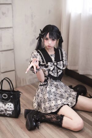 Medium kneeling shot of model wearing black lace socks and platform shoes with plaid polka dot Jirai Kei dress, showcasing skull-print handbag accessory in vintage room