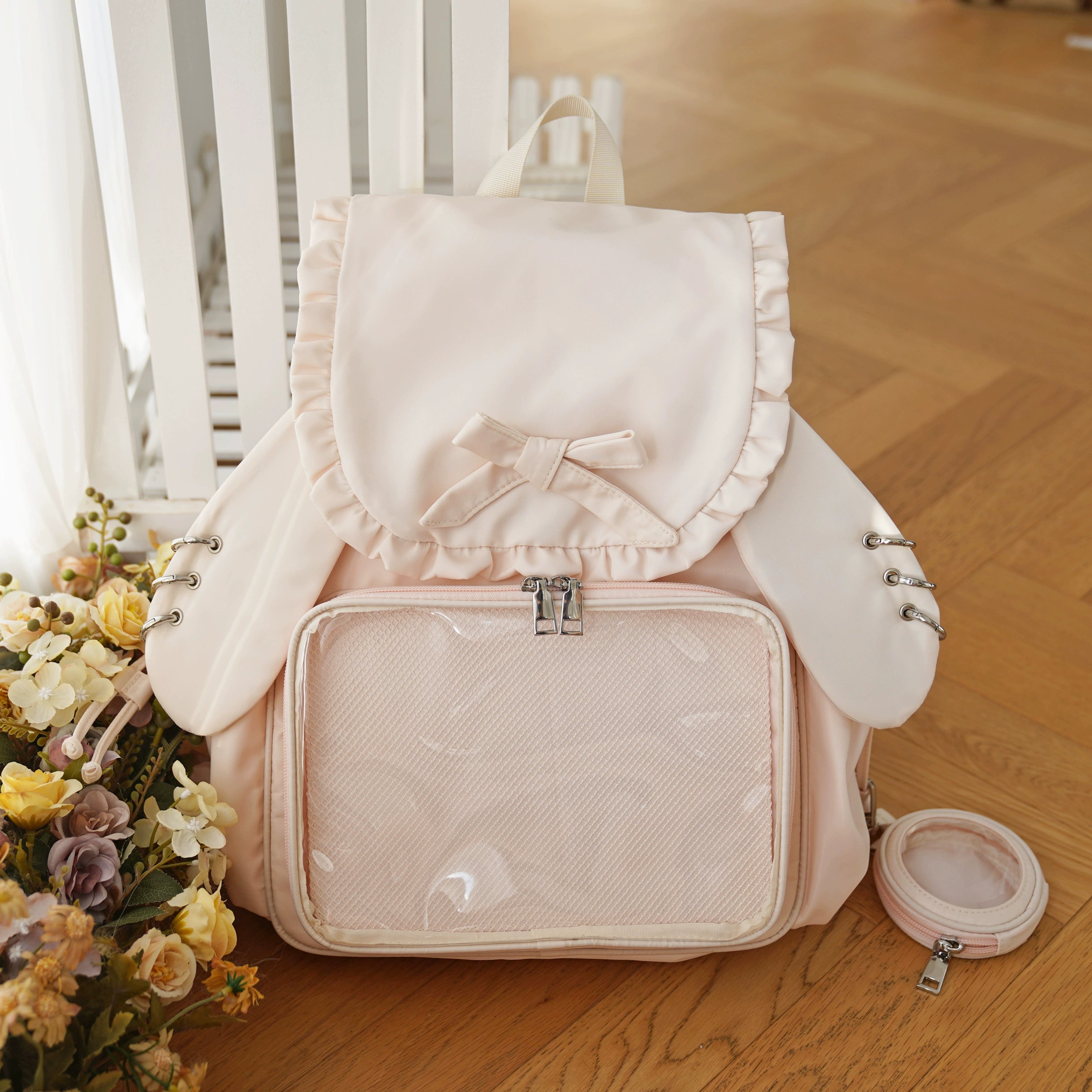 Nude pink Jirai Kei itabag backpack with playful bunny ears, transparent collectible display pocket, ruffled bow accent, and matching pouch