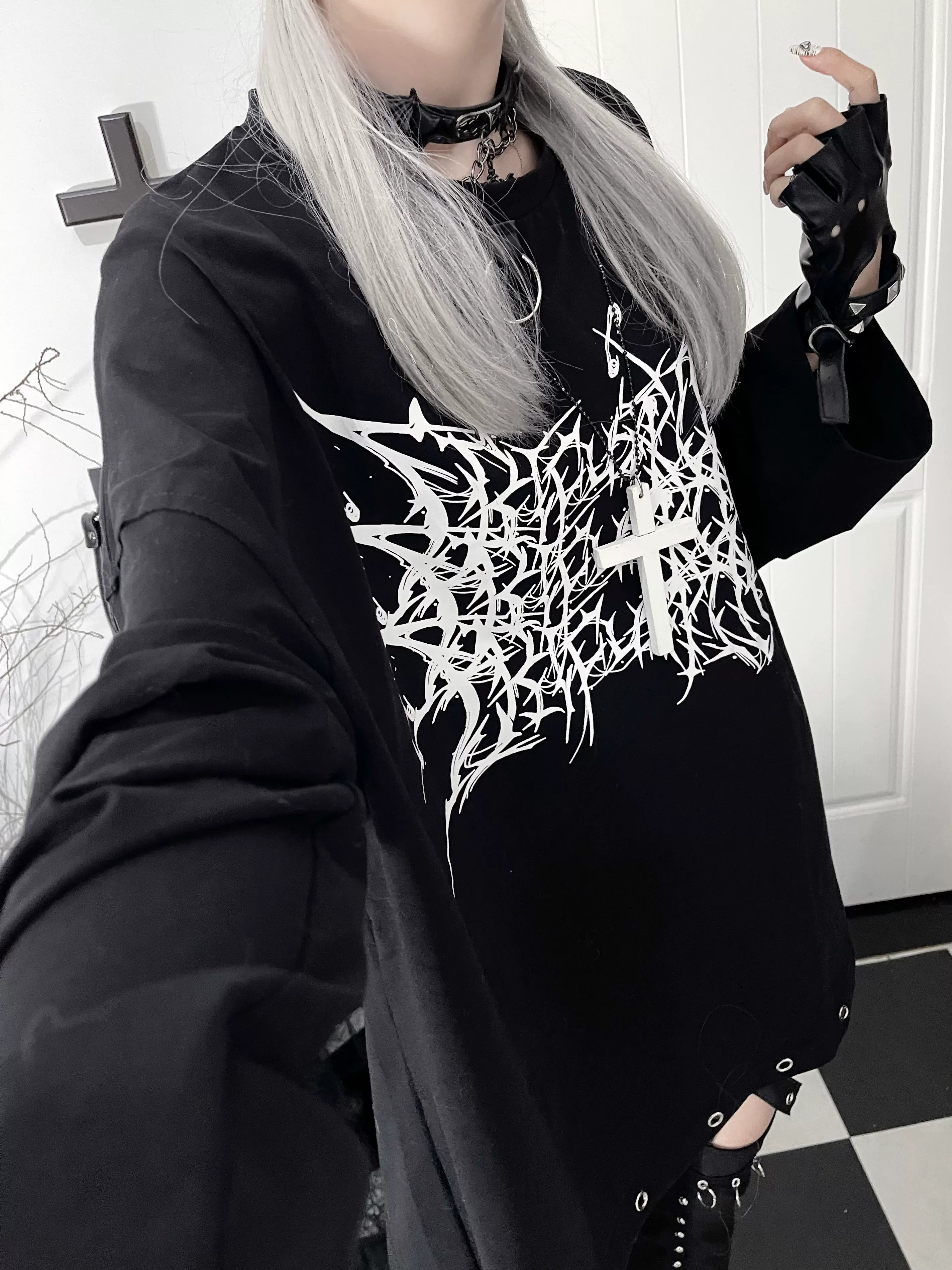 Close-up selfie of black jirai kei gothic long-sleeve tee with white thorn cross print, worn with spiked choker and fingerless gloves for dark aesthetic styling
