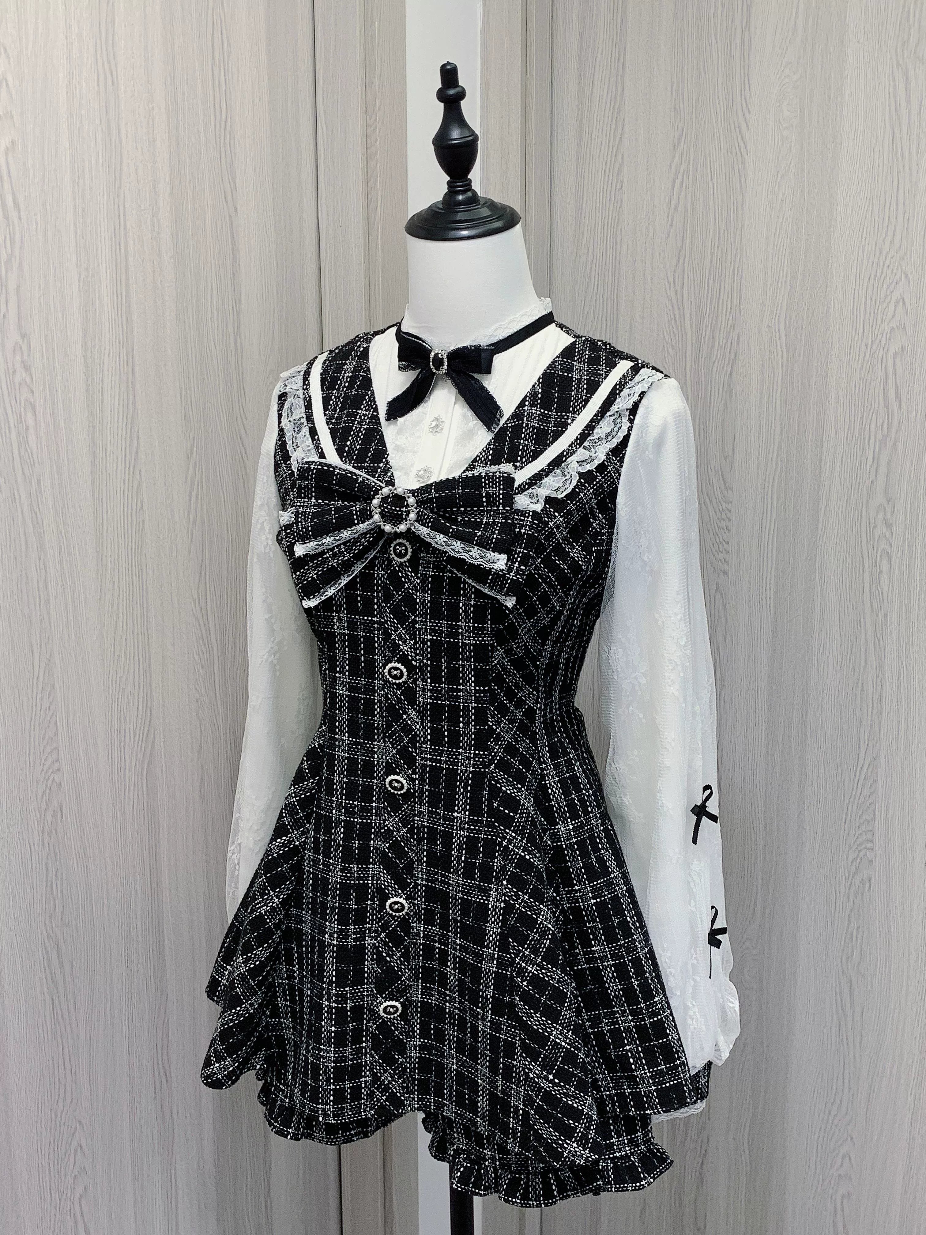 Black and white plaid Jirai Kei dress with double-layer chiffon sleeves, Peter Pan lace collar, detachable velvet bow, front button closure, and matching ruffle hem shorts - front three-quarter view on mannequin