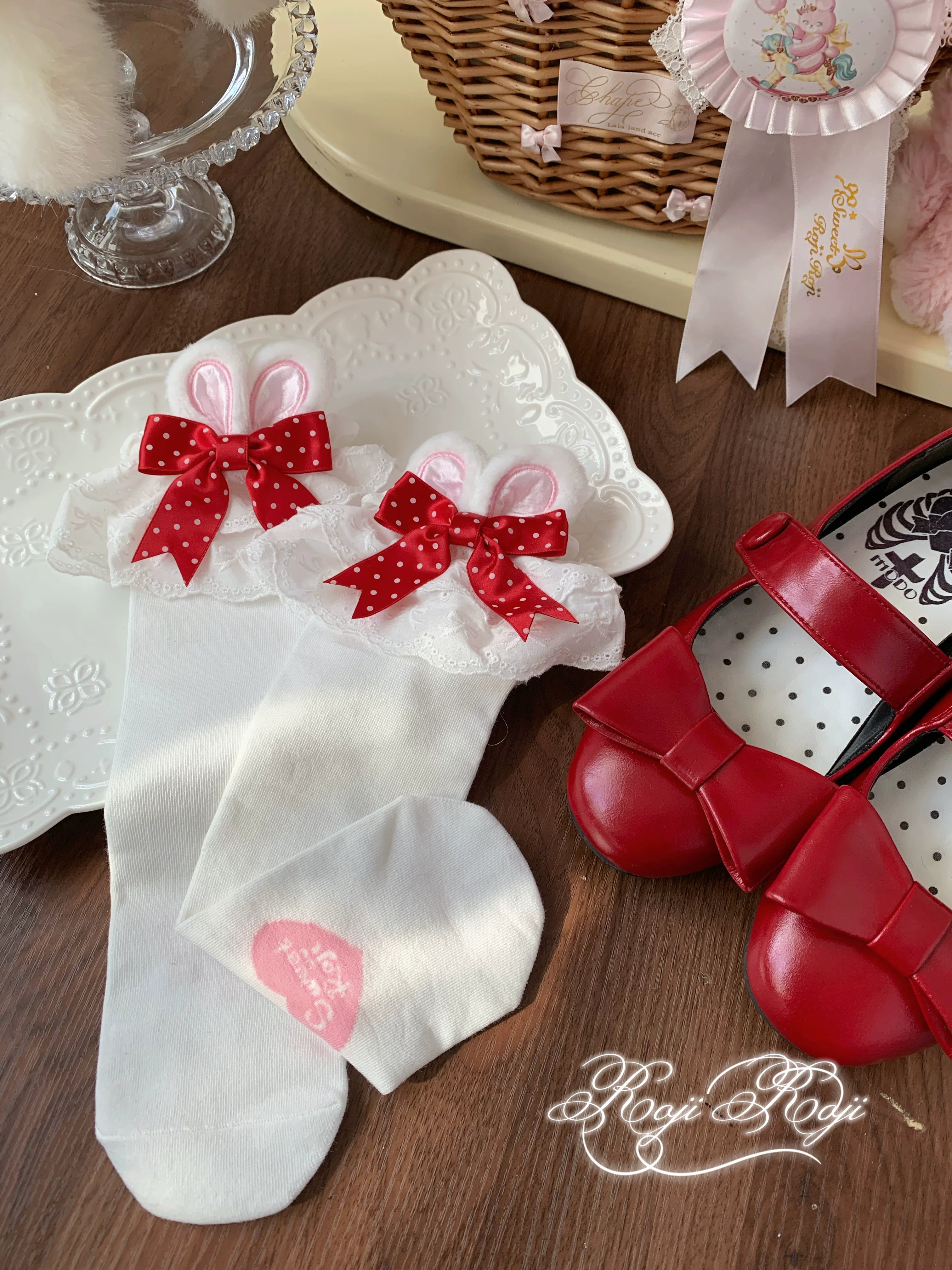 Close-up top-down view of Jirai Kei pink polka dot bunny ear socks held by hand with lace trim and plush toys in background