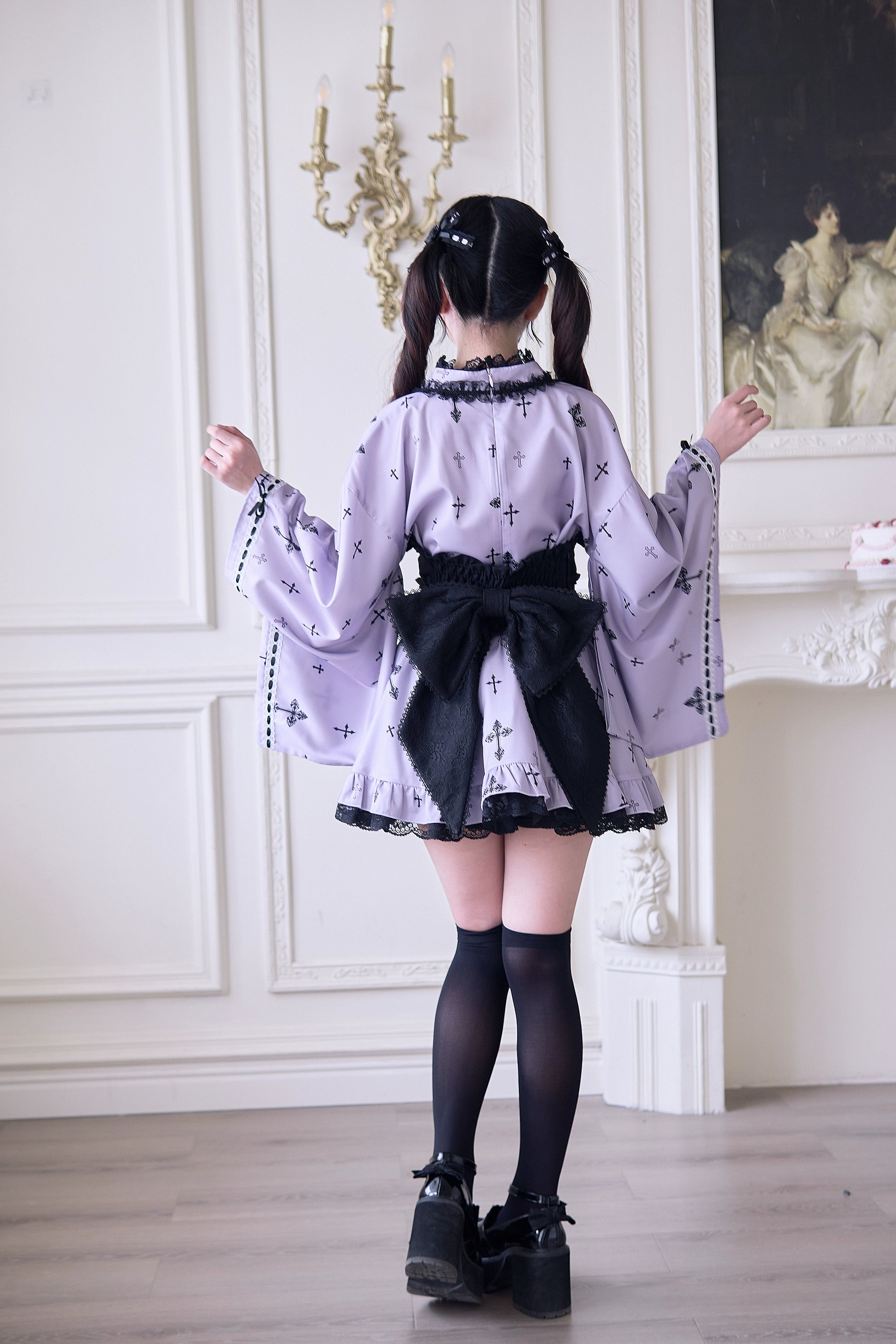Lavender Jirai Kei kimono outfit back view showing large dramatic black back bow and cross printed fabric with ruffled skirt hem in vintage parlor setting